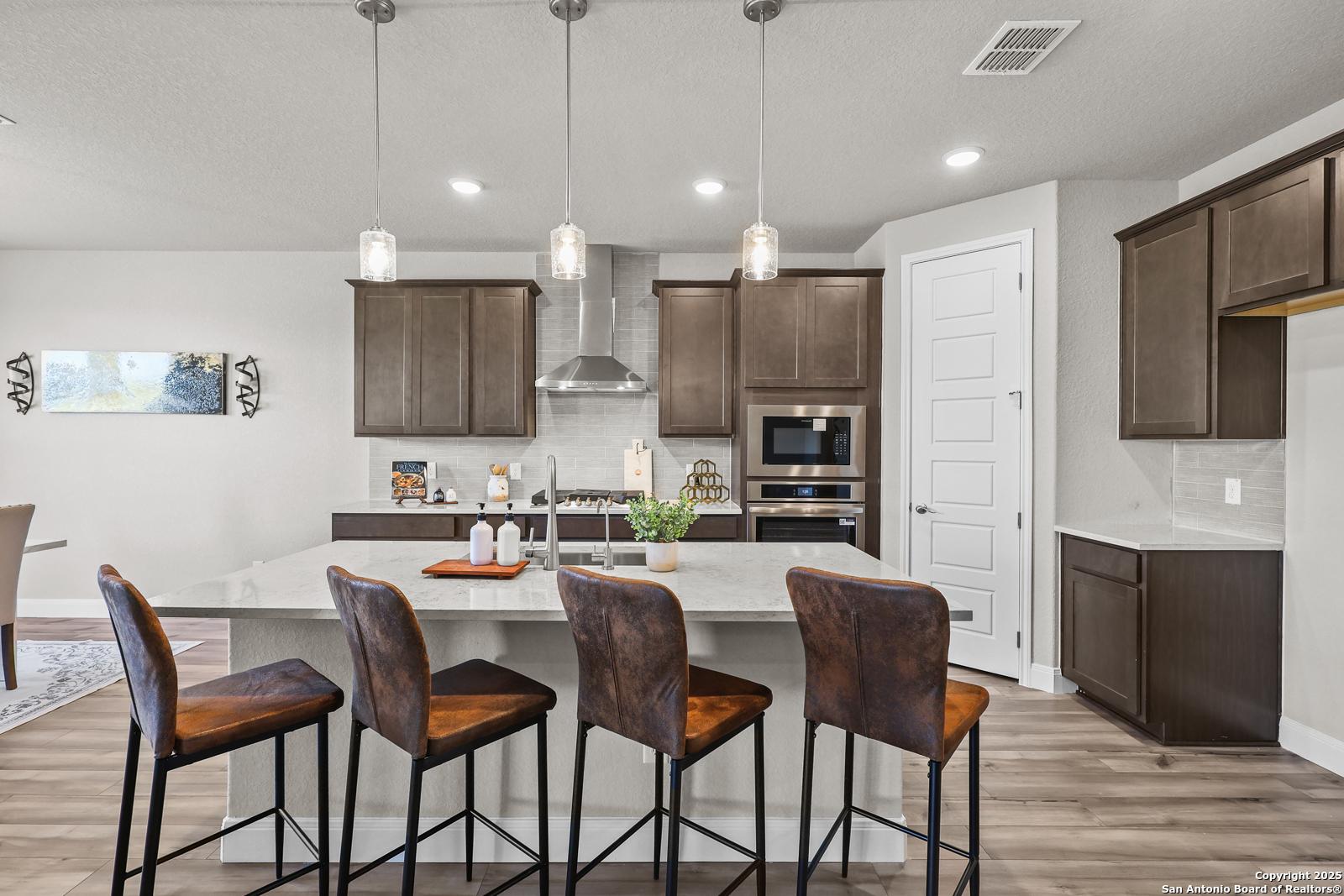 Modern kitchen with large island, leather bar stools, shaker cabinets, and stainless double ovens in The Jennings G, Castroville, Texas