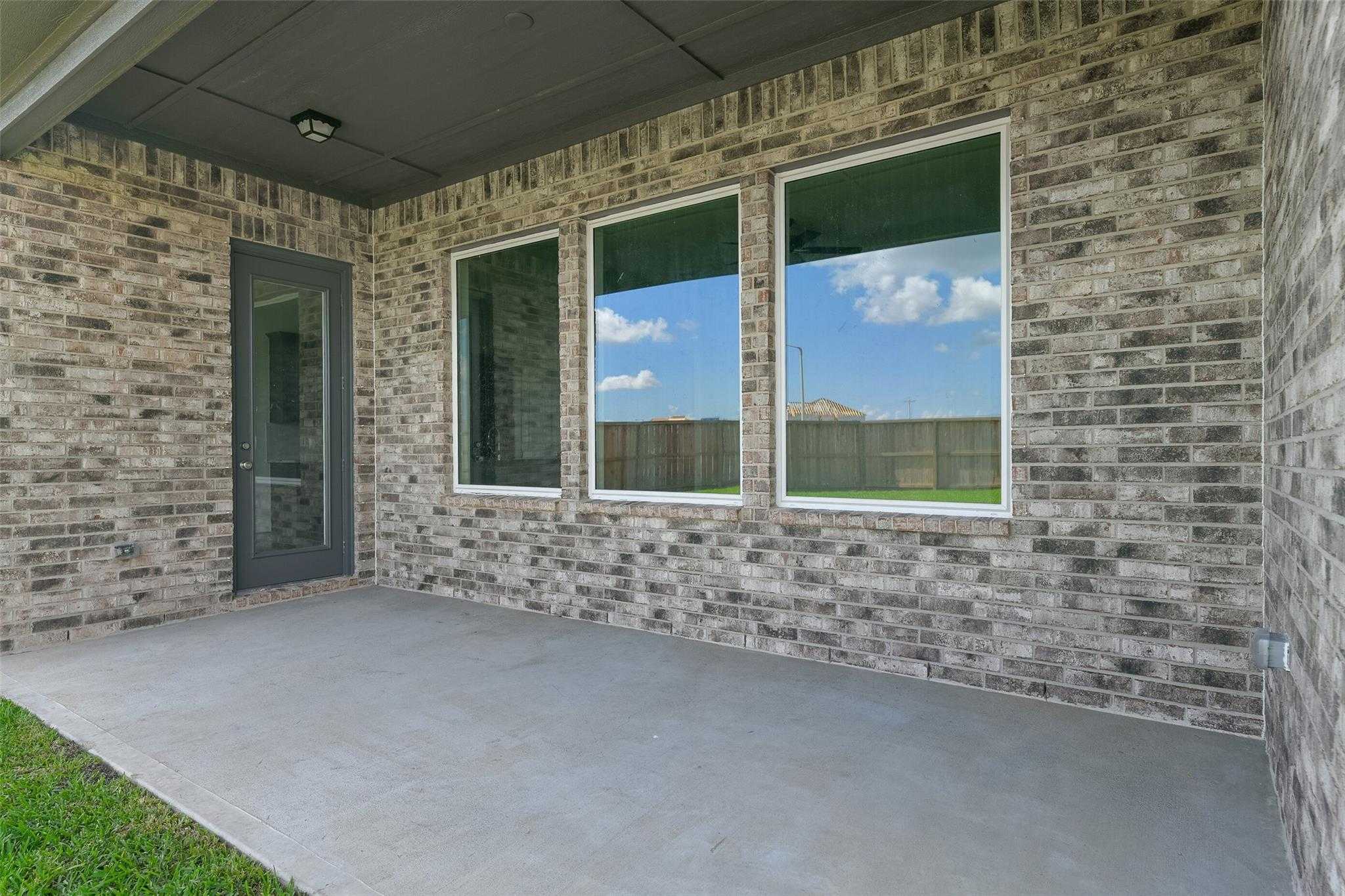 Covered back patio with large windows, brick exterior, and grassy yard in Davidson Homes The Edward A, Lago Mar, Texas City