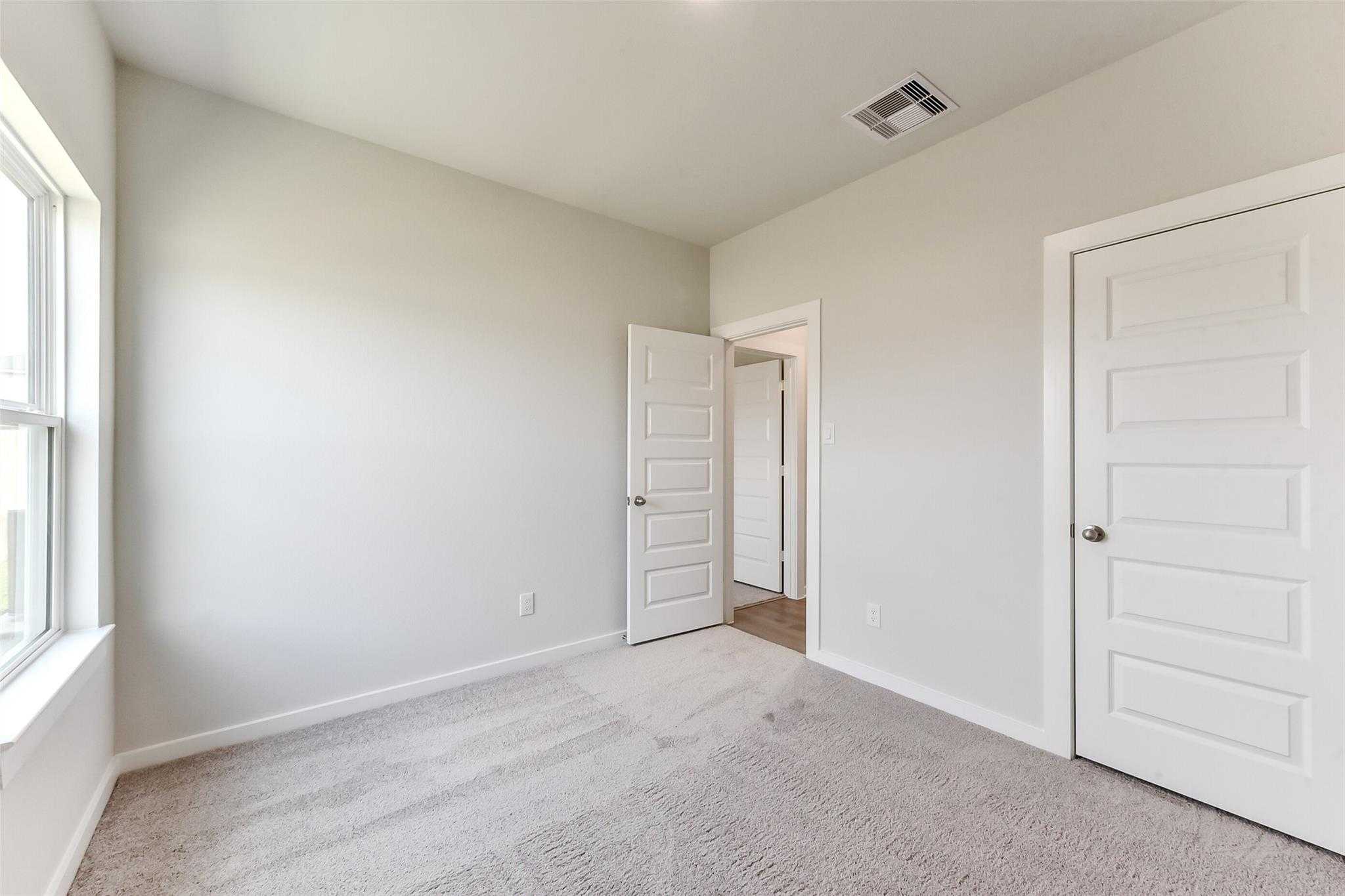 Empty secondary bedroom with light gray walls, neutral carpet, large windows, and open doorway in Davidson Homes The Frio F, Dayton, Texas