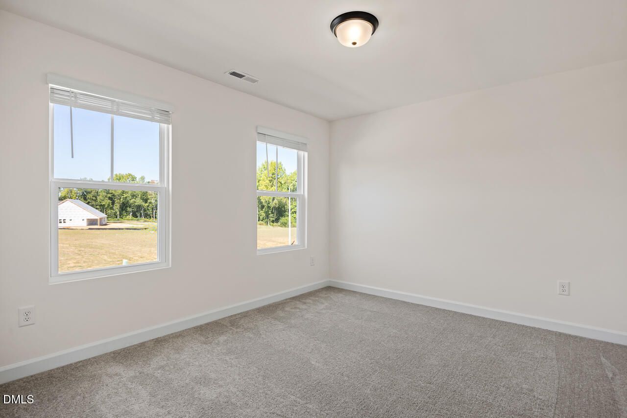 Bright carpeted bedroom with dual windows overlooking scenic views in Davidson Homes The Hickory II B, Lillington, North Carolina