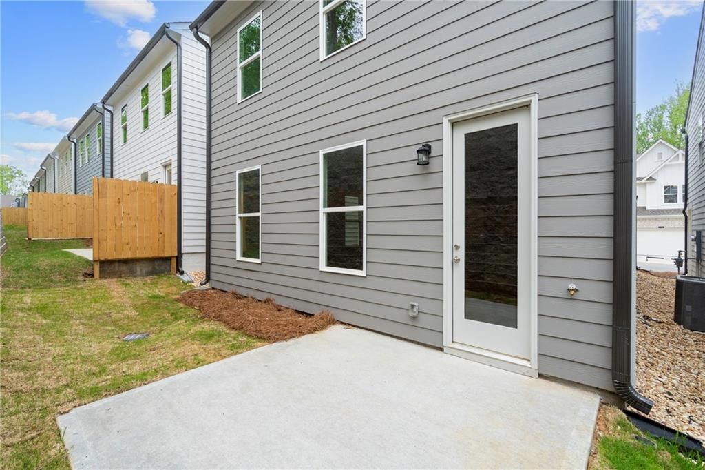 Two-story gray-sided home exterior with glass side door, windows, concrete patio, wooden fence, and landscaped yard in The Village at Shallowford, Kennesaw, Georgia