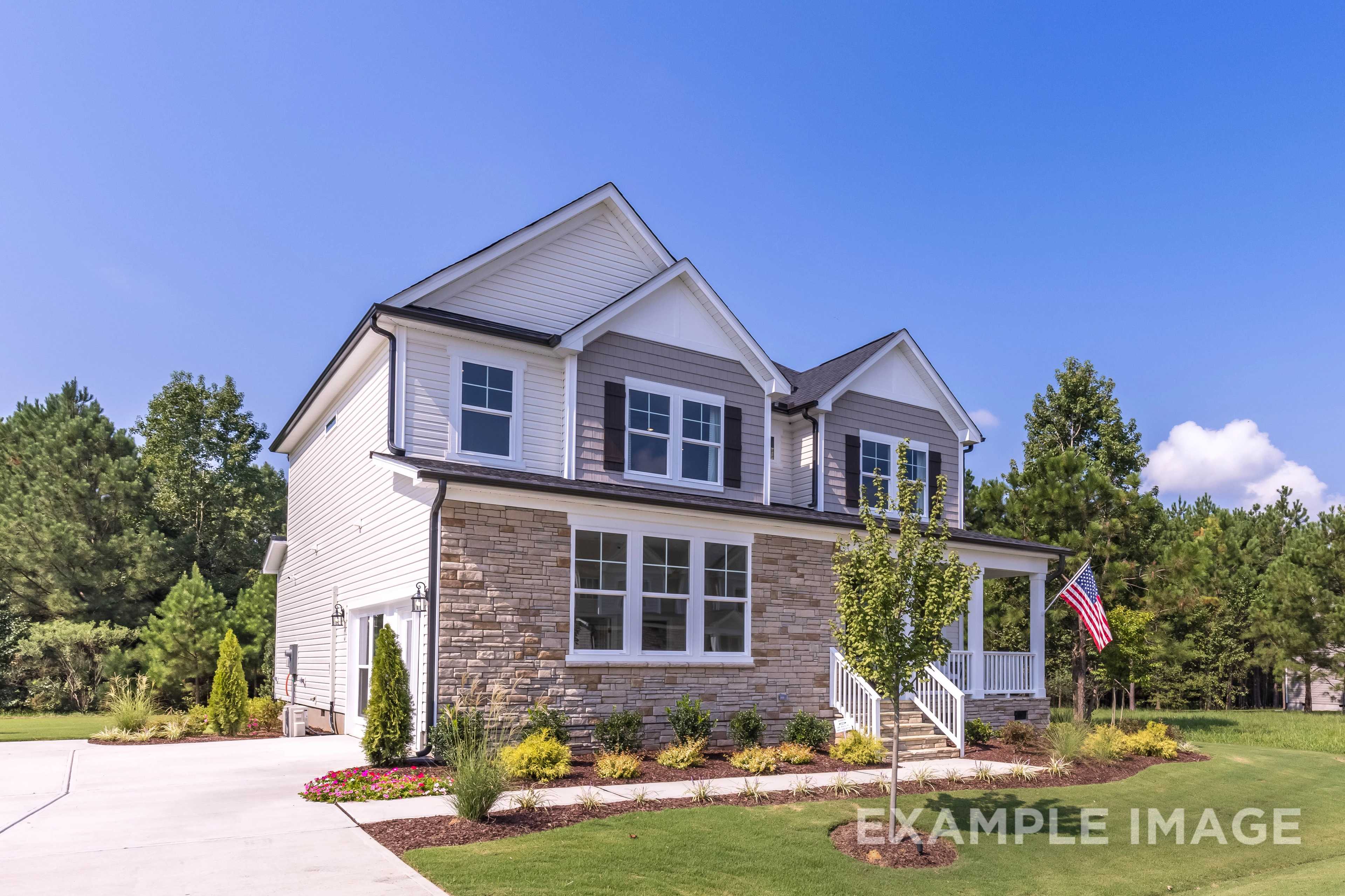Charming two-story The Willow B facade with stone base, white siding, front porch, American flag, and landscaped yard in Wendell NC