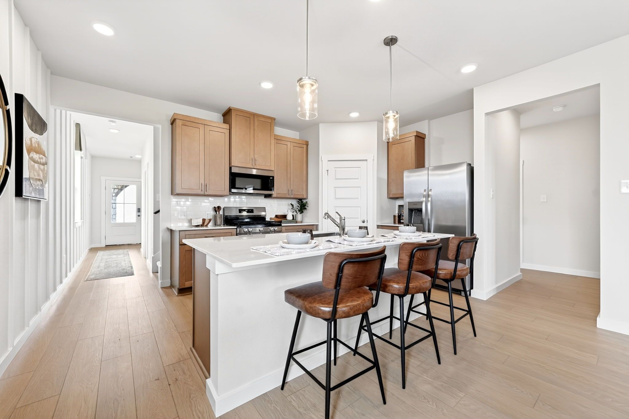 Modern kitchen at Mesa Vista in San Antonio by Davidson Homes with quartz island, leather bar stools, and wood cabinetry.