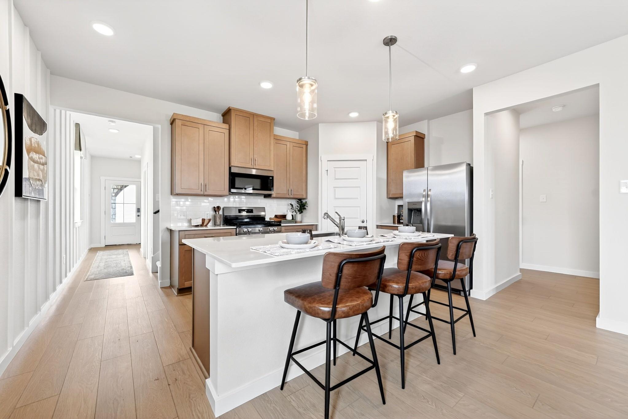 Modern kitchen at Mesa Vista in San Antonio by Davidson Homes with quartz island, leather bar stools, and wood cabinetry.