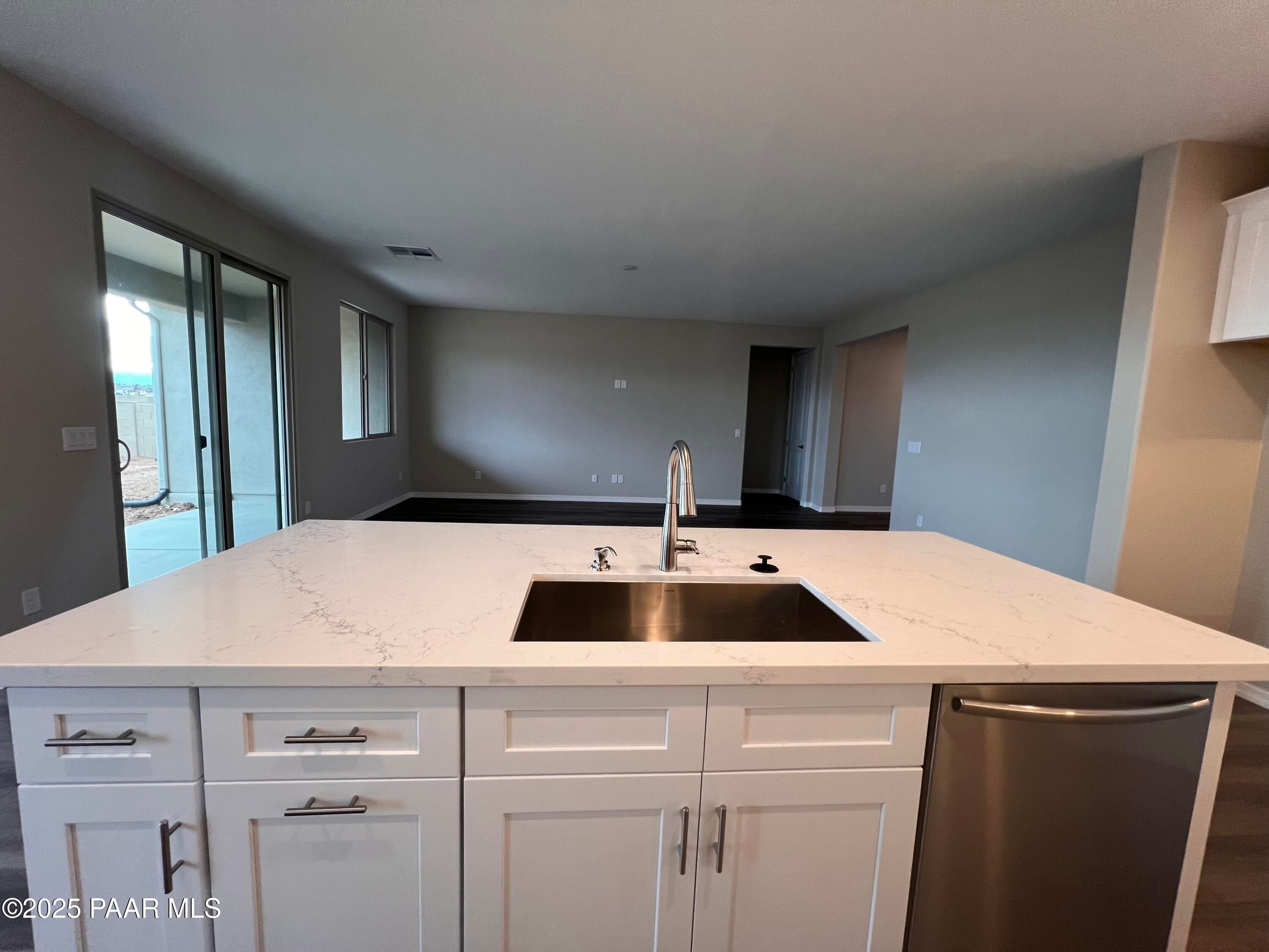 Modern kitchen with large quartz island, stainless sink, white cabinets, open to living area in Davidson Homes The Harmony A, Prescott Valley, AZ