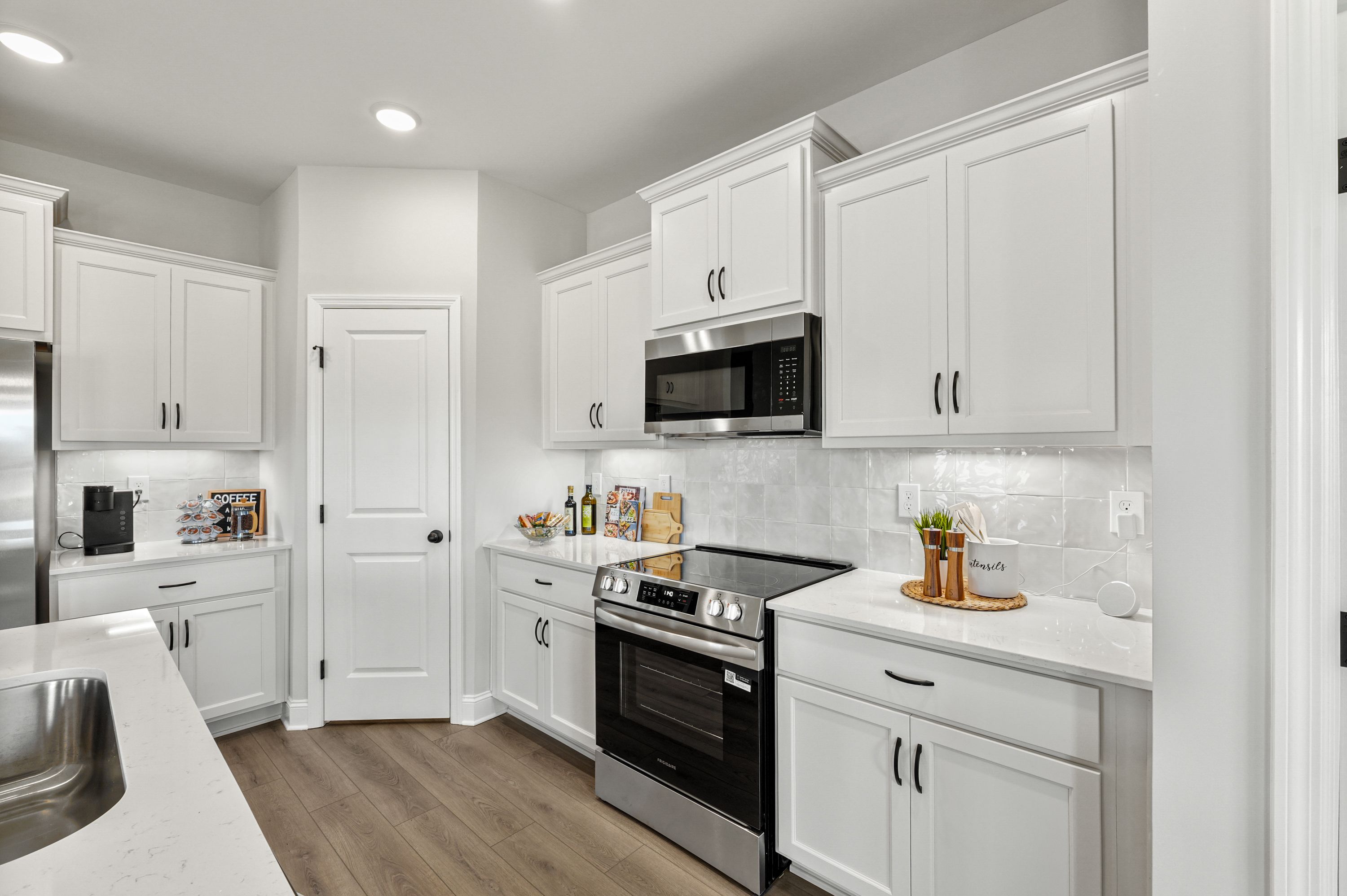 Spacious modern kitchen in Ramsay Cove, Owens Cross Roads AL with white shaker cabinets, stainless steel appliances, quartz island, and hardwood floors