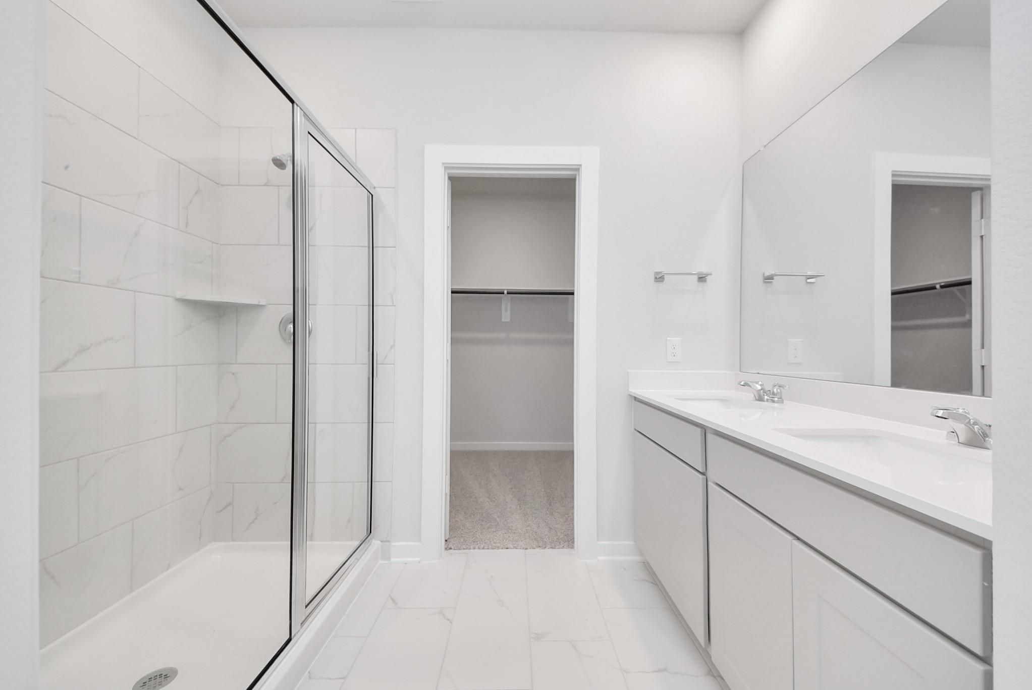 Modern primary bathroom with walk-in shower, double vanity, and walk-in closet in Davidson Homes The Blanco F, Conroe, TX.