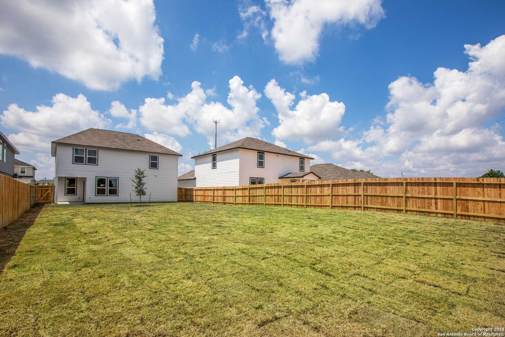 Spacious green backyard with wooden privacy fence behind two-story white home, Davidson Homes Murray H, Hannah Heights, Seguin, Texas
