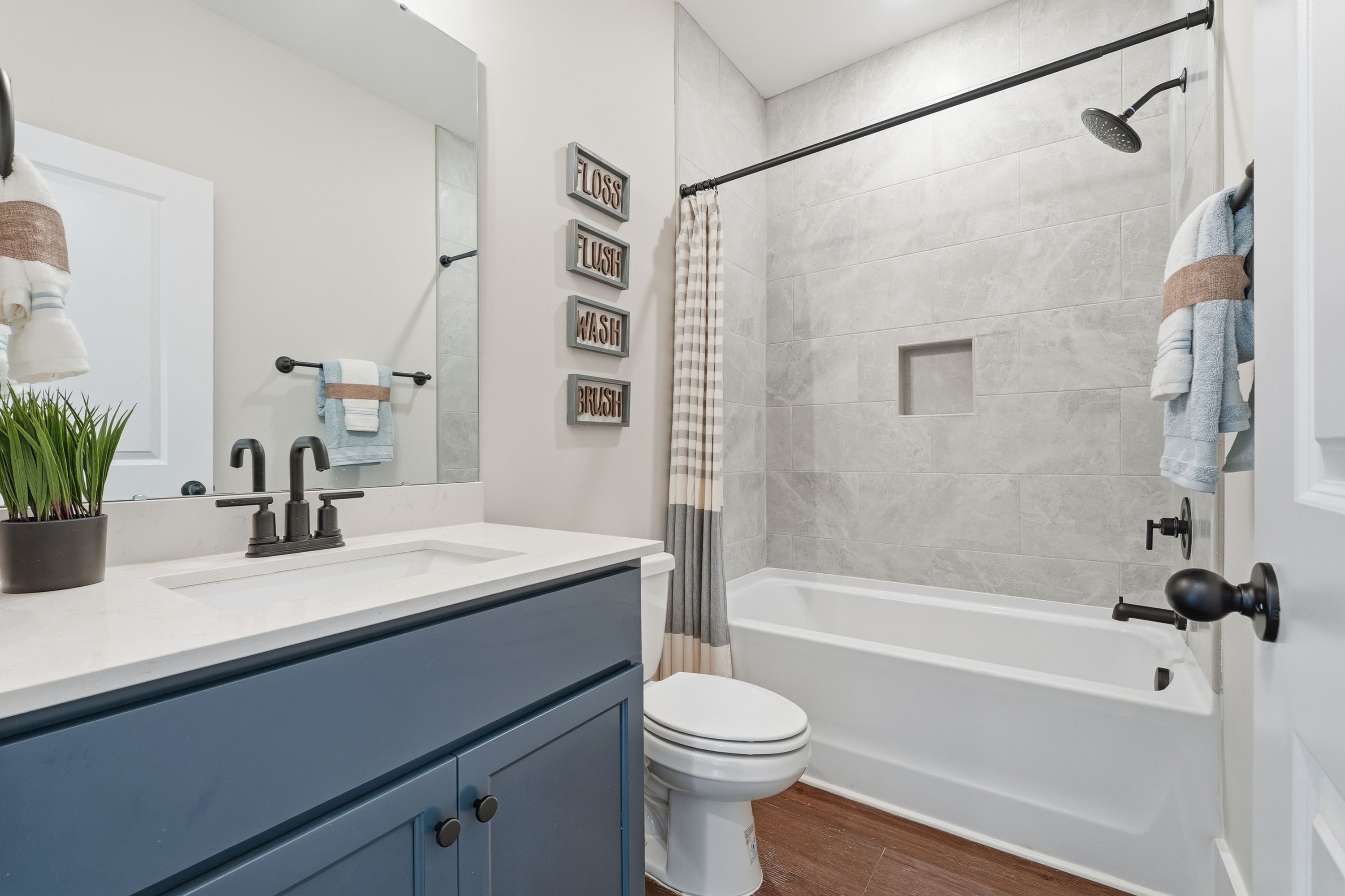 Spacious bathroom at Noble Ridge in Cullman Alabama with bathtub shower combo, blue vanity, and hardwood floors