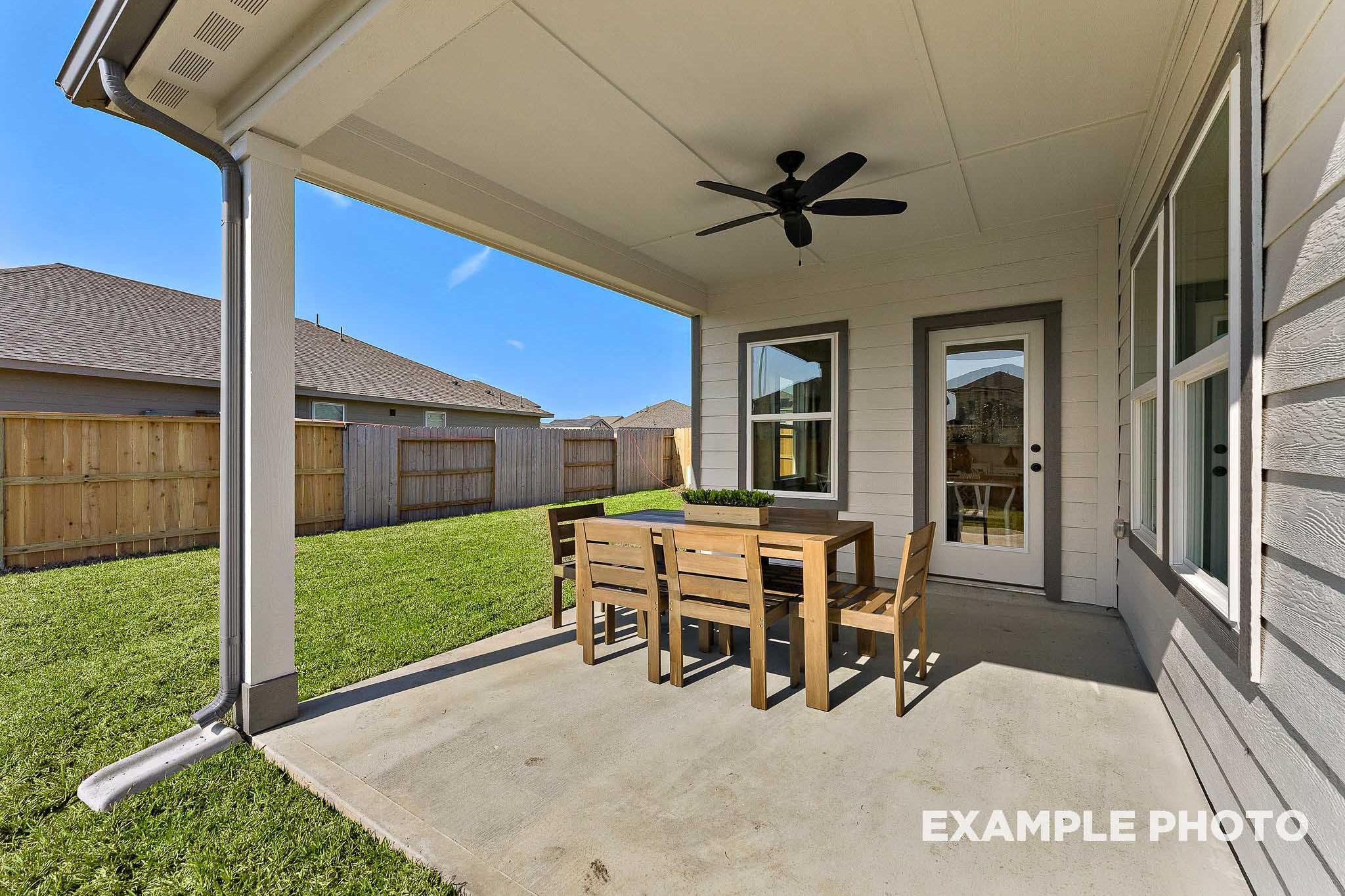 Spacious covered patio of The Everett E home design with wooden dining table, chairs, ceiling fan, and glass doors overlooking lush backyard