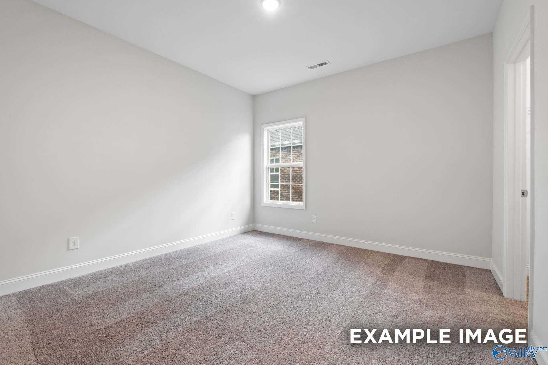 Bright empty bedroom with light gray walls, beige carpet, and large window in Davidson Homes The Montgomery, Athens AL