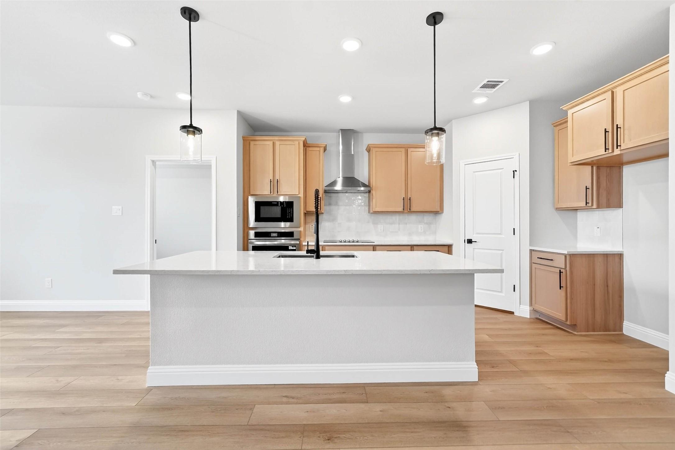 Modern kitchen with white island, light wood cabinets, and stainless steel appliances in The Holly C plan, Anna, Texas.
