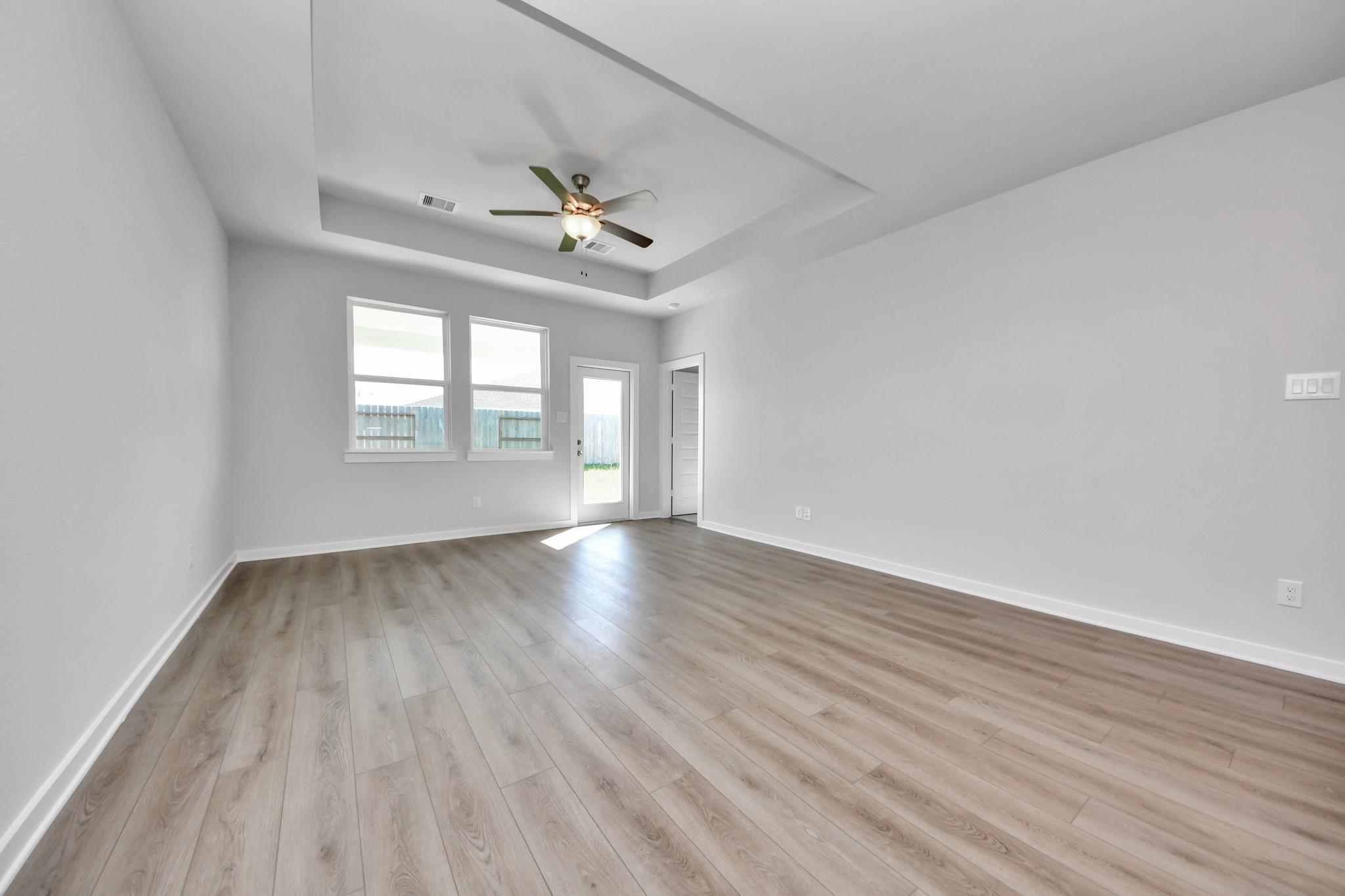 Spacious living room with tray ceiling, ceiling fan, and wood-look flooring in The Colorado G home at Emberly in Beasley.