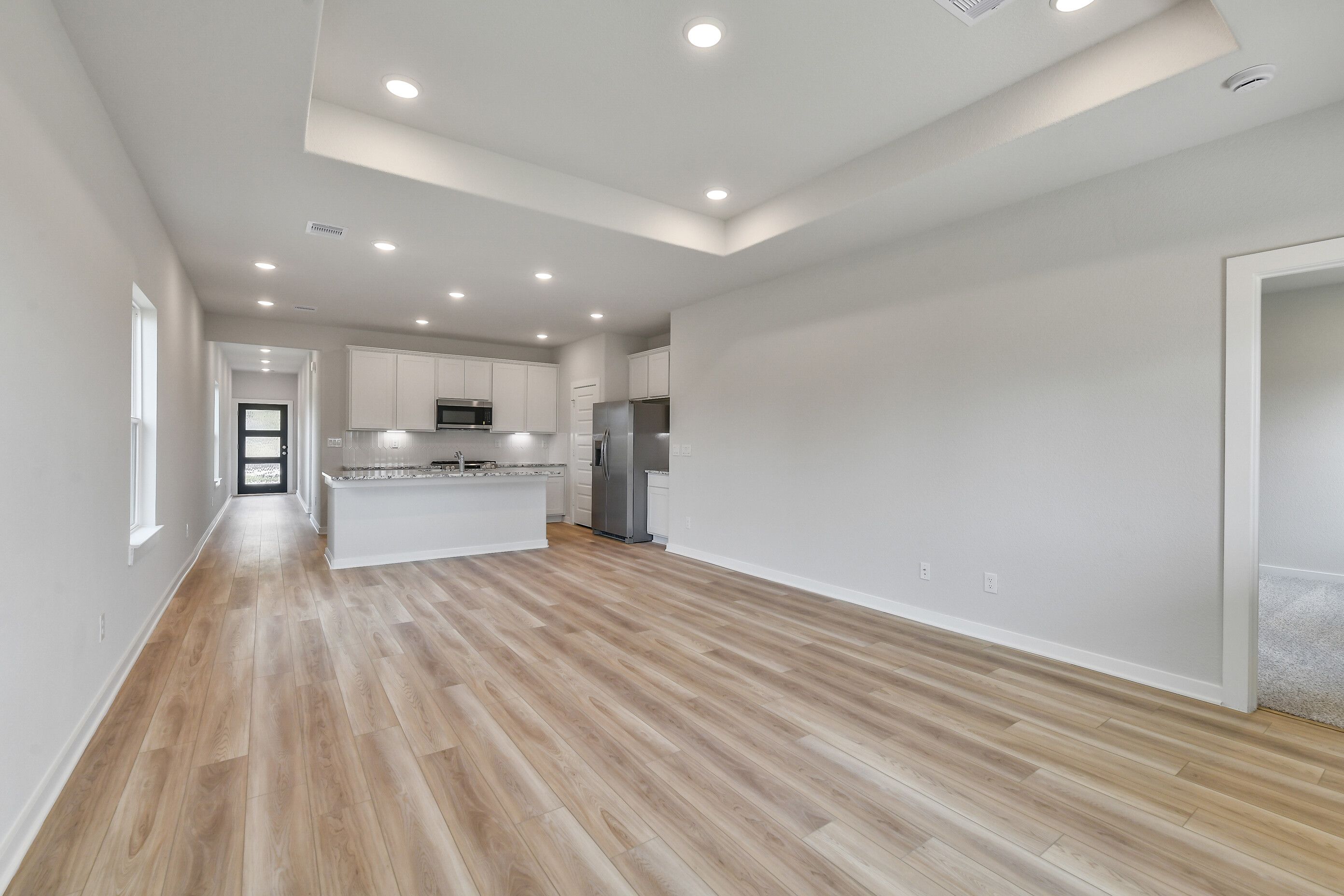 Open-concept kitchen with white cabinets, stainless steel fridge and microwave, luxury vinyl plank flooring in Davidson Homes The Colorado G, Magnolia TX