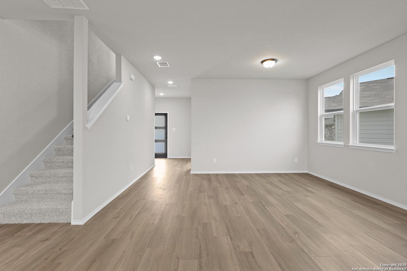 Bright open foyer with staircase, light oak floors, and large windows in The Murray J 4-bedroom home, Royal Crest, San Antonio