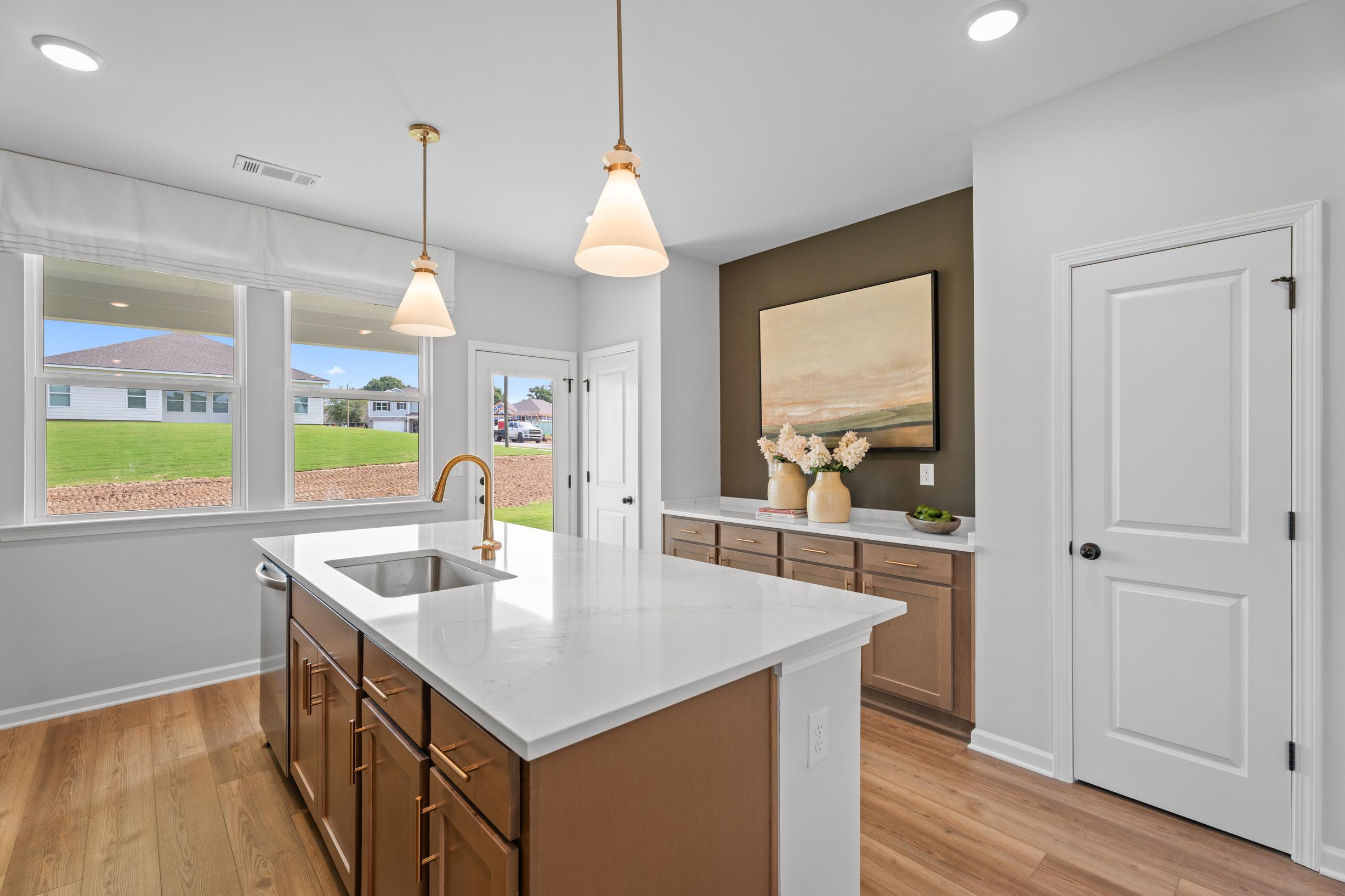 Modern kitchen with quartz island, wood cabinetry, and pendant lighting at Links Crossing in Auburn, Alabama by Davidson Homes