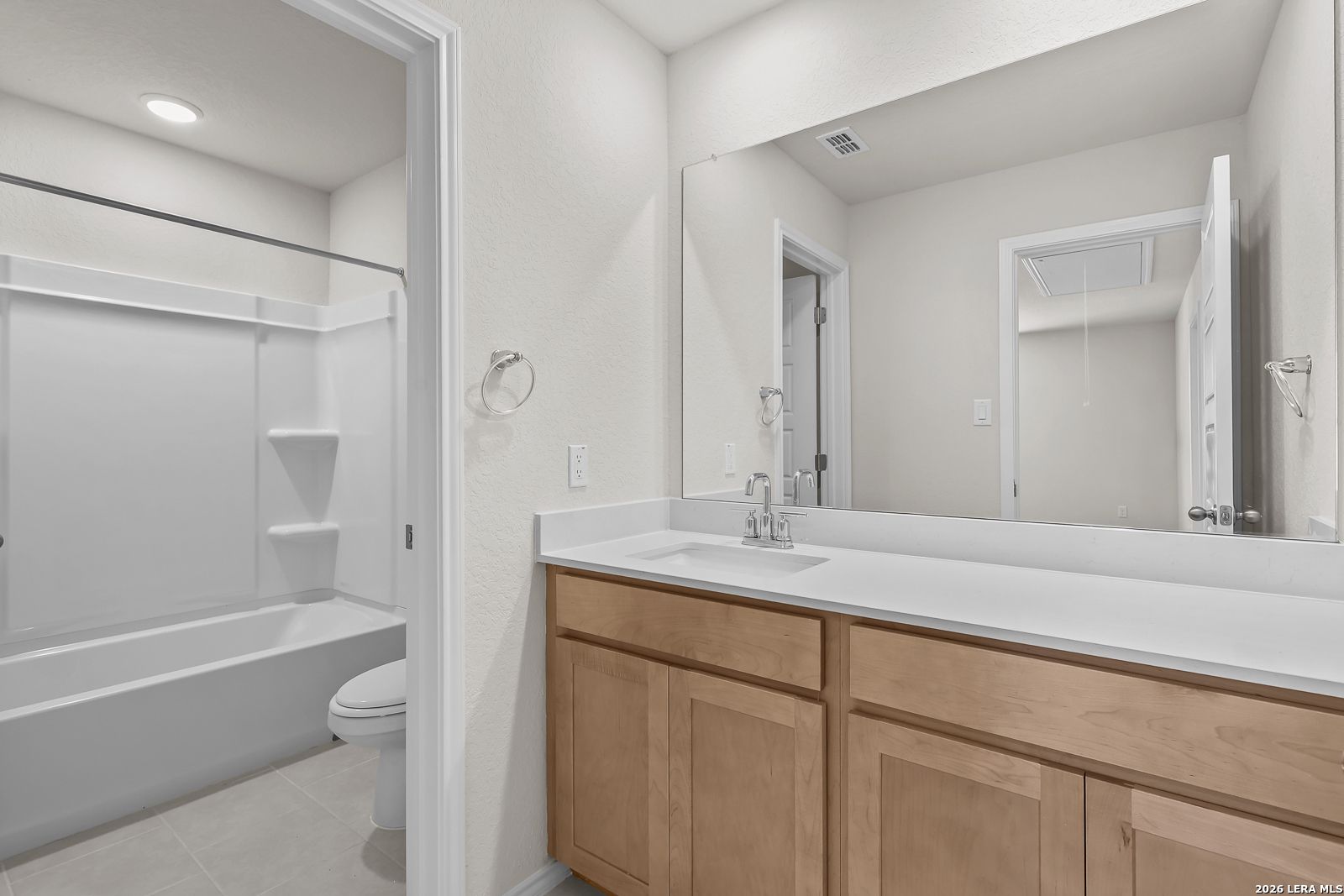 Modern bathroom with light wood vanity, white countertop, and tub-shower combo in The Gillian B at Meadows at Oak Creek.