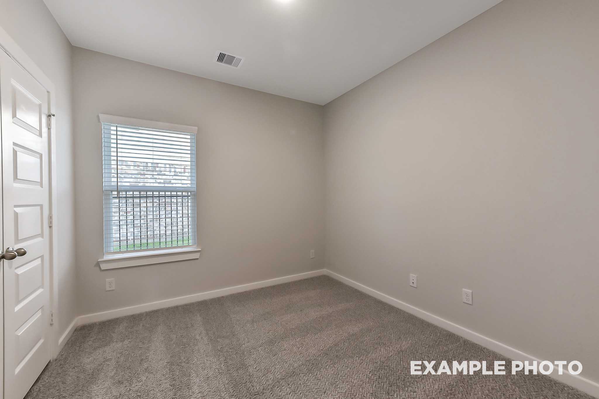 Spacious secondary bedroom in The Laguna B home with beige walls, carpeted floor, large window blinds, and white door