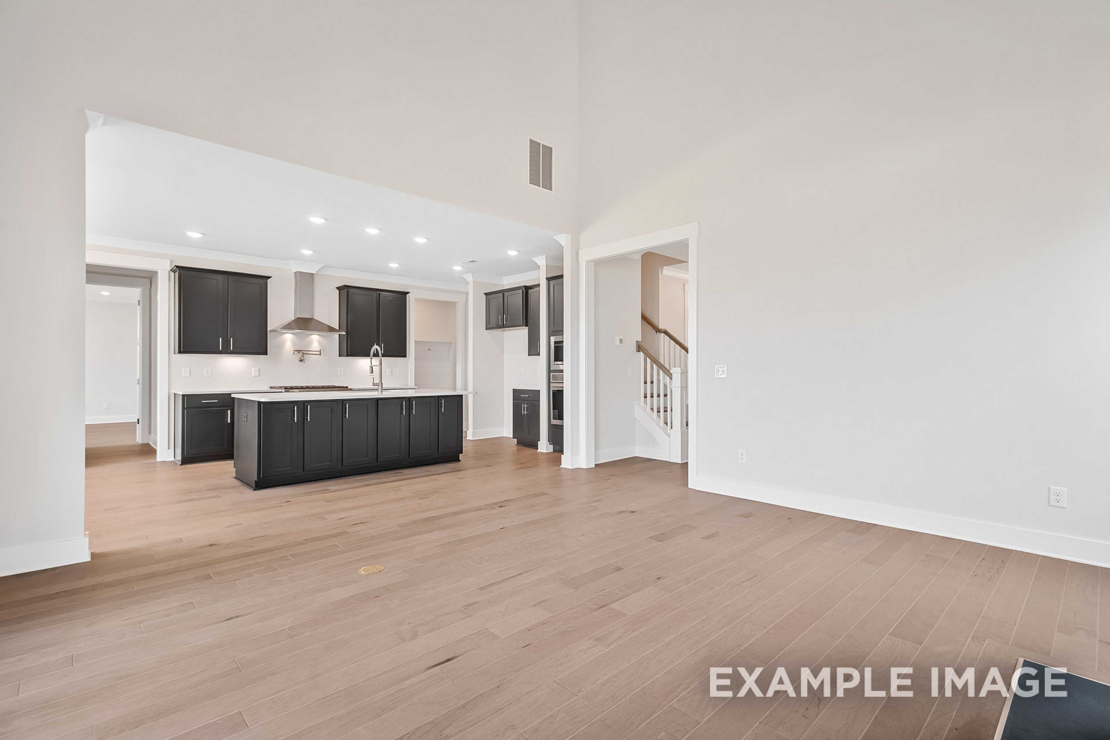 Spacious open-concept kitchen in The Hawkins with dark cabinets, large island, hardwood floors, and staircase view