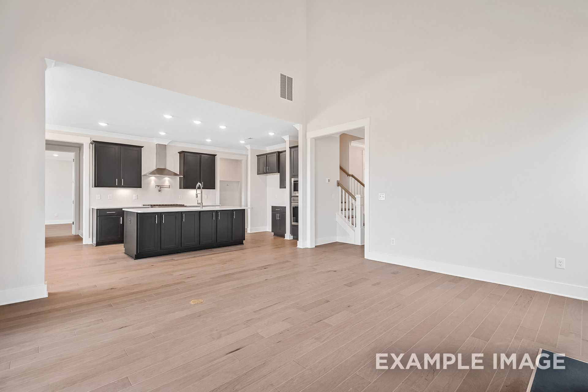 Spacious open-concept kitchen in The Hawkins with dark cabinets, large island, hardwood floors, and staircase view
