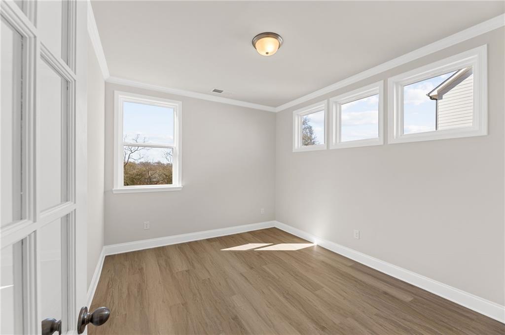 Bright empty bedroom with light gray walls, hardwood floors, and large windows in Davidson Homes The Willow B, Hoschton, Georgia