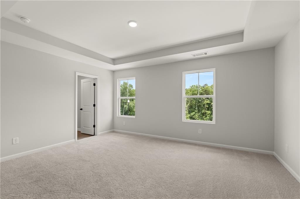 Spacious bedroom with tray ceiling and neutral carpet in The Hartwell A floor plan at The Bluffs in Canton, Georgia.