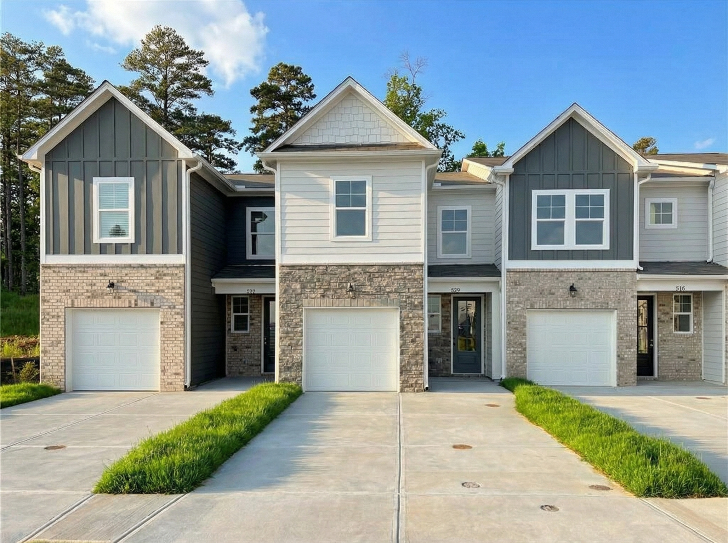 Three 2-story townhomes with gray siding, brick bases, garages, and landscaped driveways in Stegall Village, Emerson, Georgia Davidson Homes Wilmington B