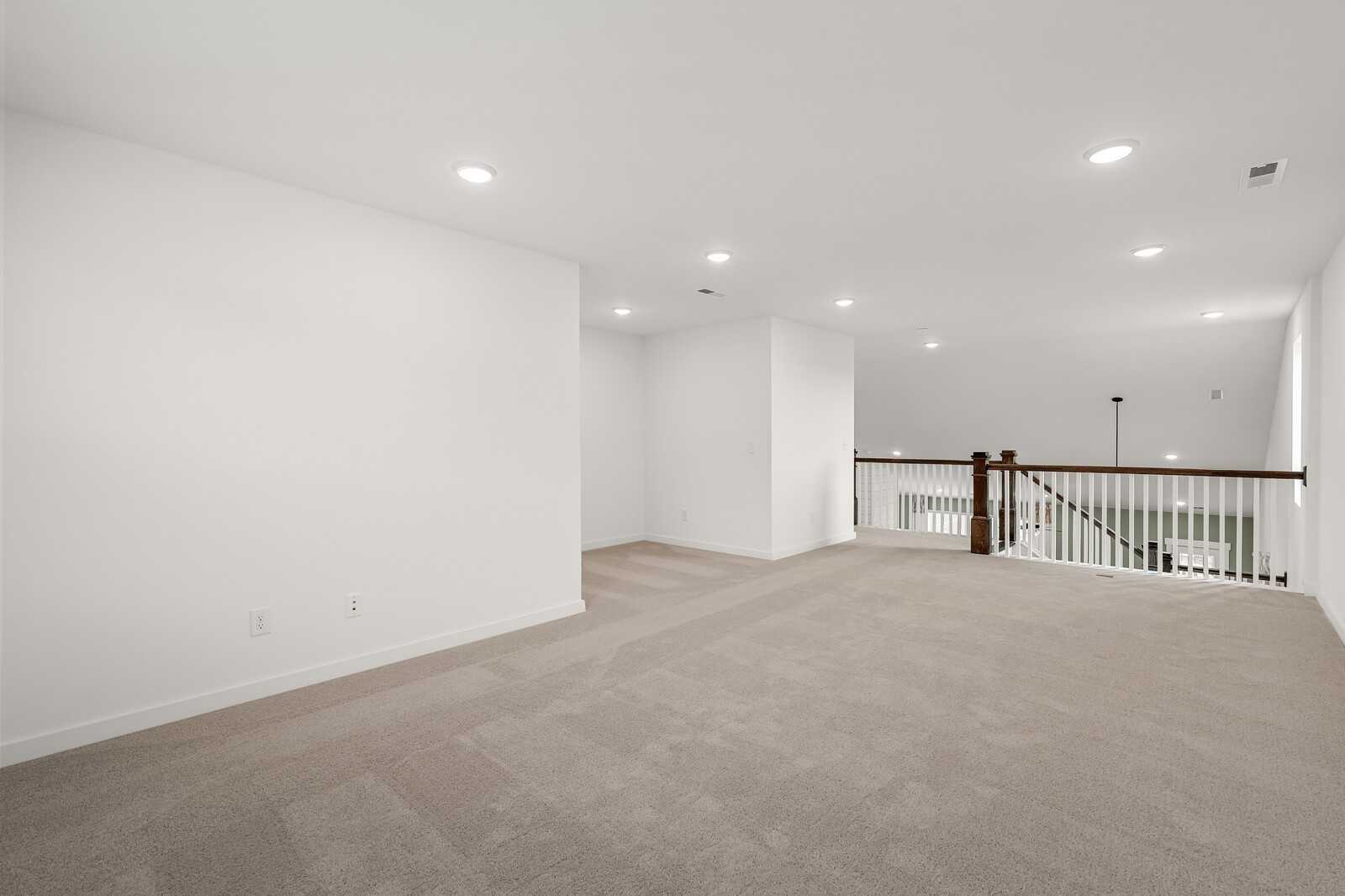 Spacious upstairs loft with beige carpet, white walls, recessed lights, and wooden railing overlook in Davidson Homes The Ridgeport, Gallatin, TN