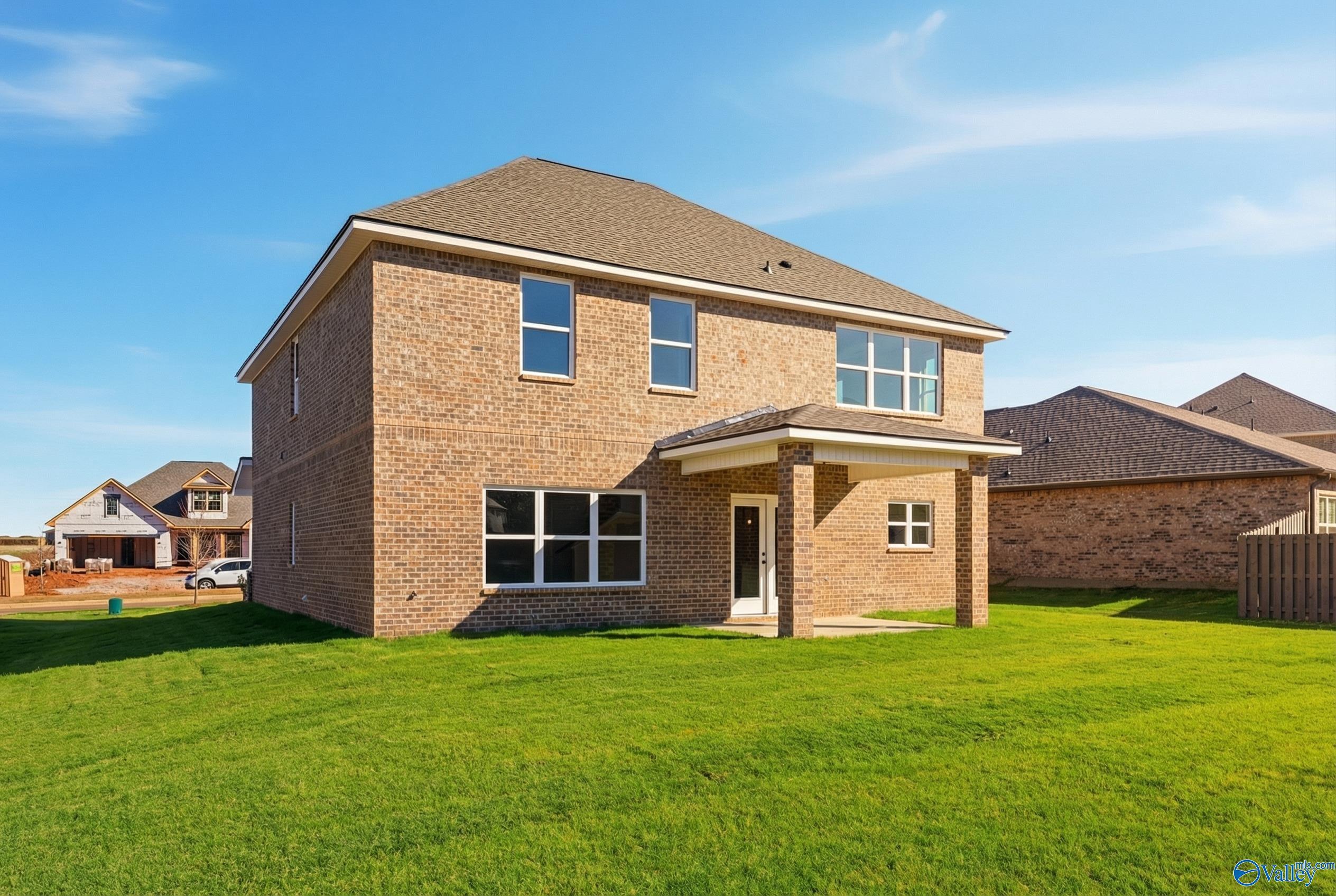 Two-story brick 4-bedroom home with covered front porch, 2-car garage, and lush green yard in Creekside, Harvest, Alabama