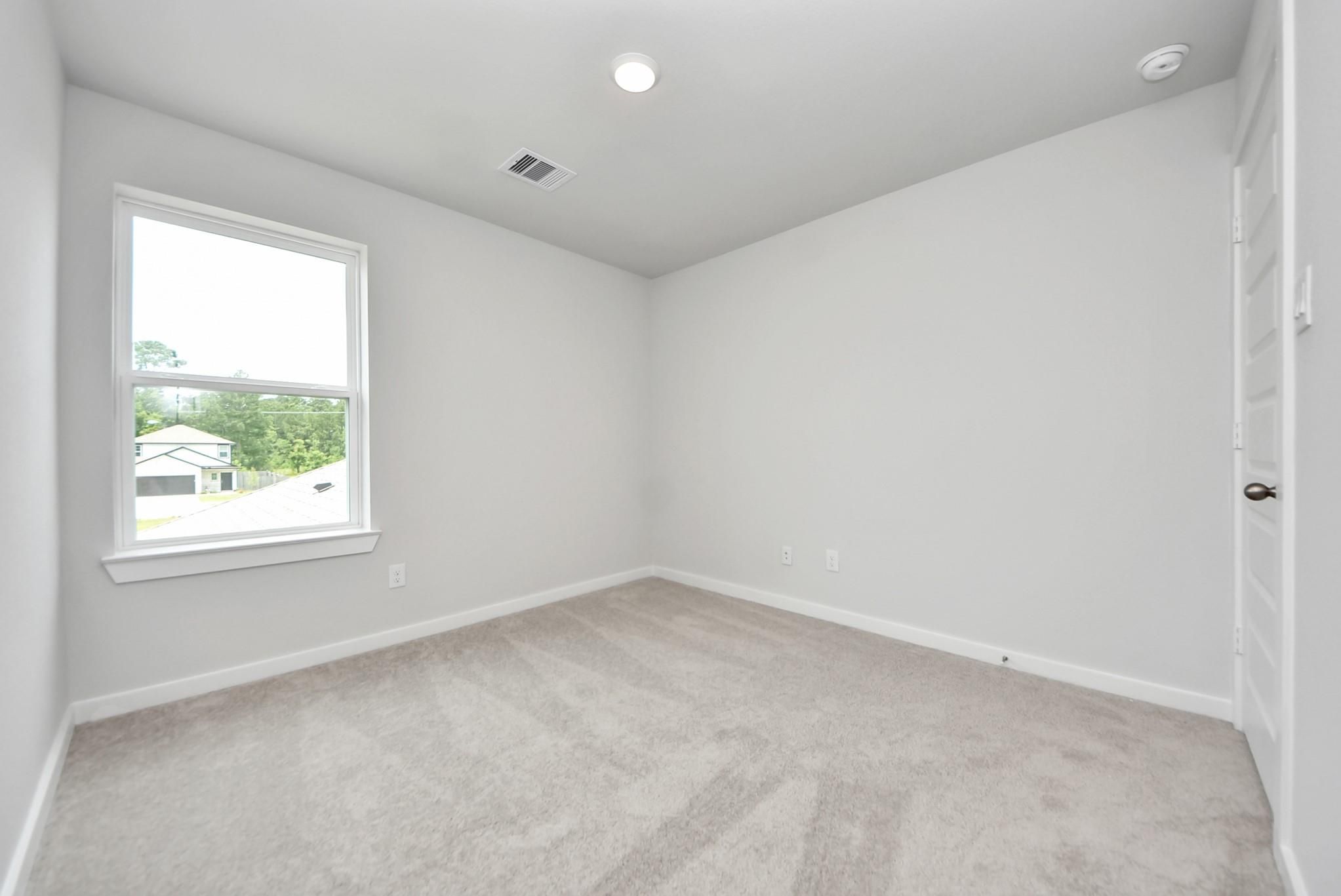 Bright, carpeted bedroom with neutral walls in The Blanco E floor plan at The Villages at WestPointe in Dayton, Texas.