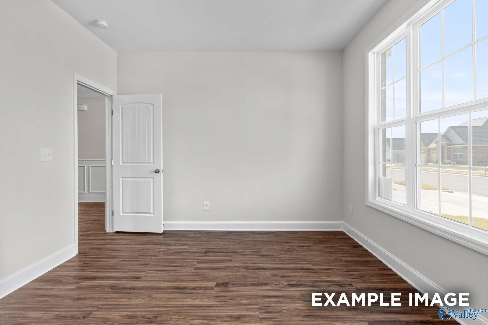 Bright empty bedroom with neutral walls, hardwood floors, open door, and large sunny windows in Davidson Homes Montgomery C, Harvest, Alabama