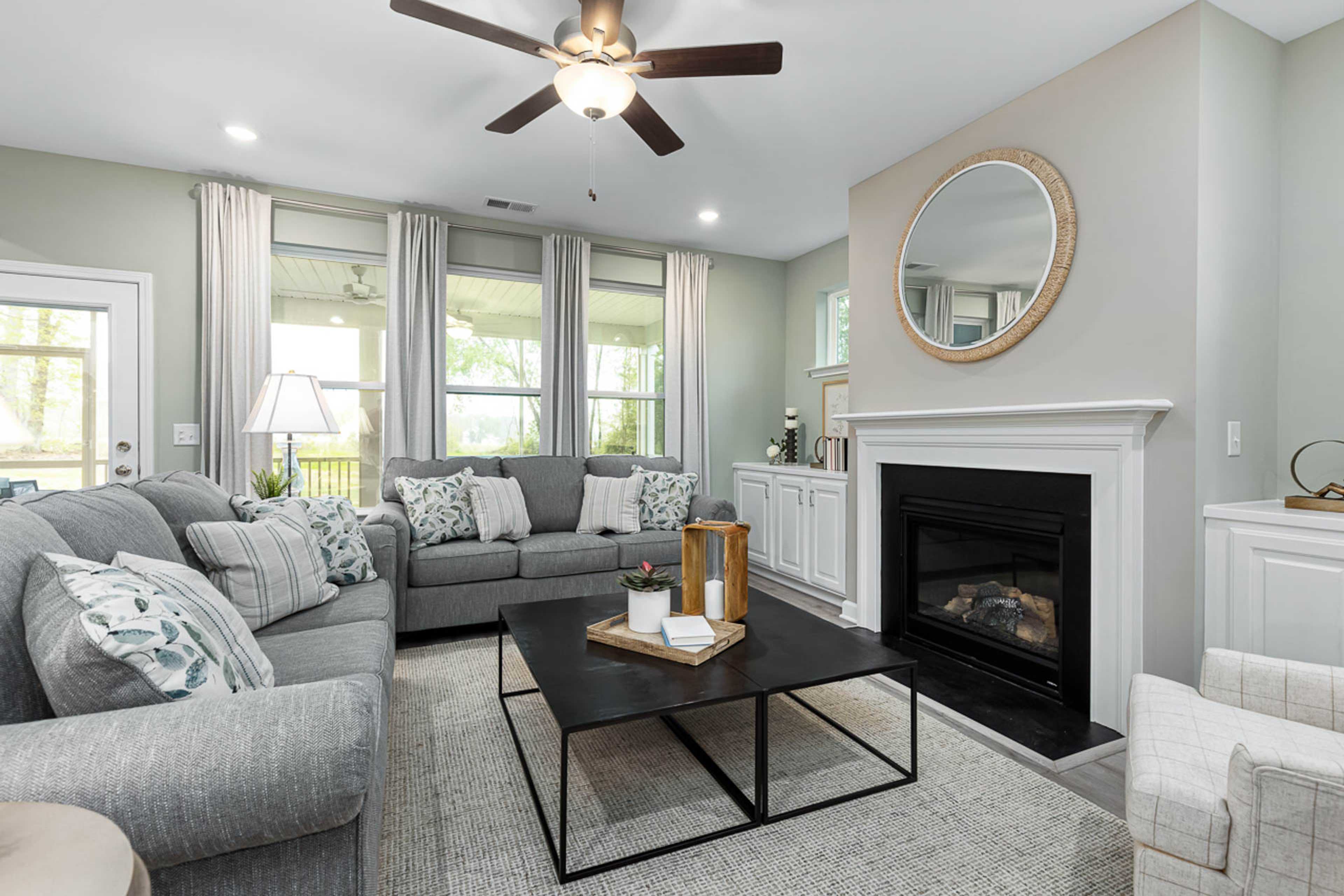 Cozy living room in Weatherford East, Angier NC by Davidson Homes with gray sectional sofa, gas fireplace, and large windows