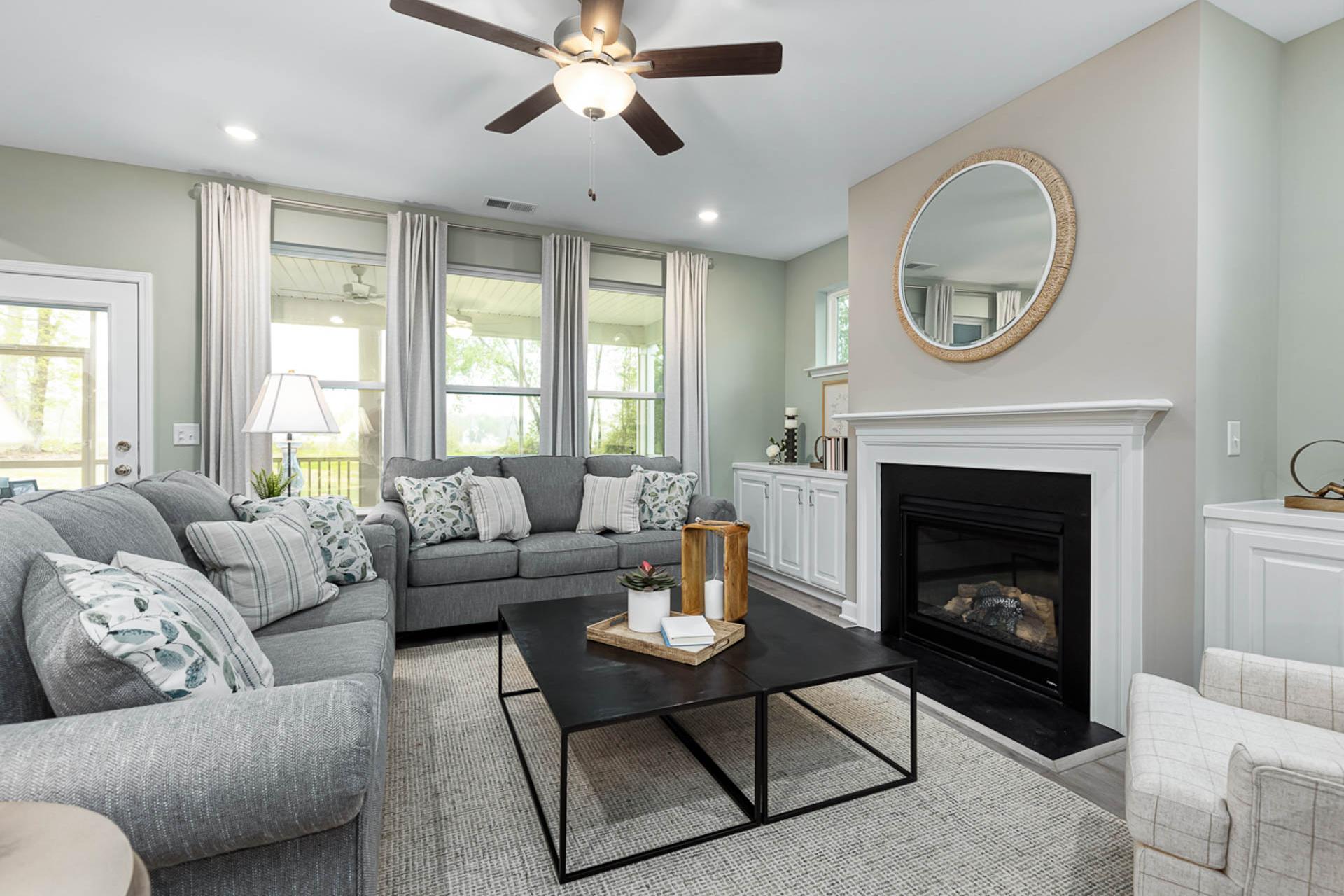 Cozy living room in Weatherford East, Angier NC by Davidson Homes with gray sectional sofa, gas fireplace, and large windows