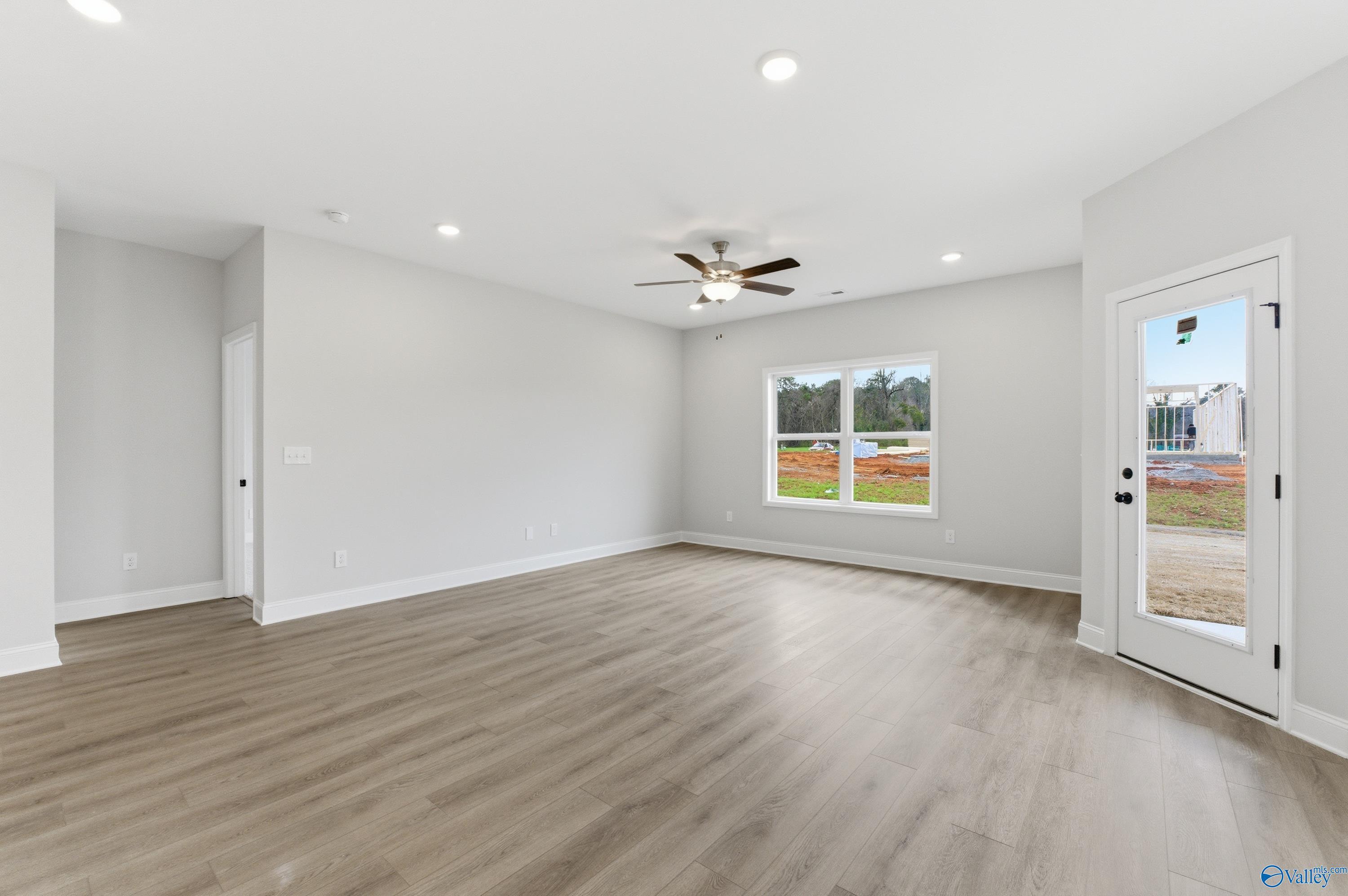 Spacious empty living room with ceiling fan, large windows, and glass door in Davidson Homes The Daphne C, Huntsville, Alabama