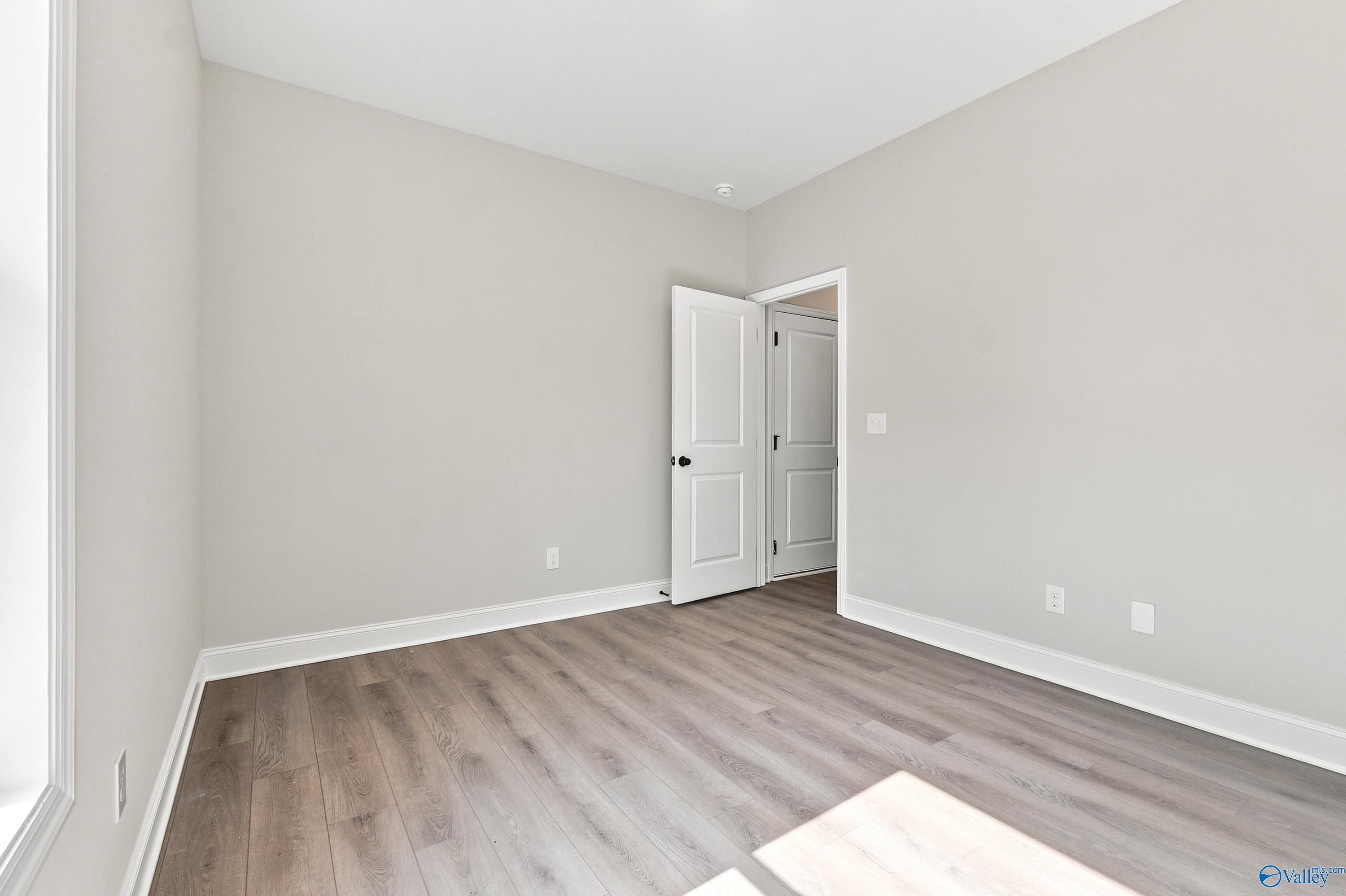Spacious bedroom with grey walls and wood-look flooring in The Daphne floor plan by Davidson Homes in Meridianville, AL.