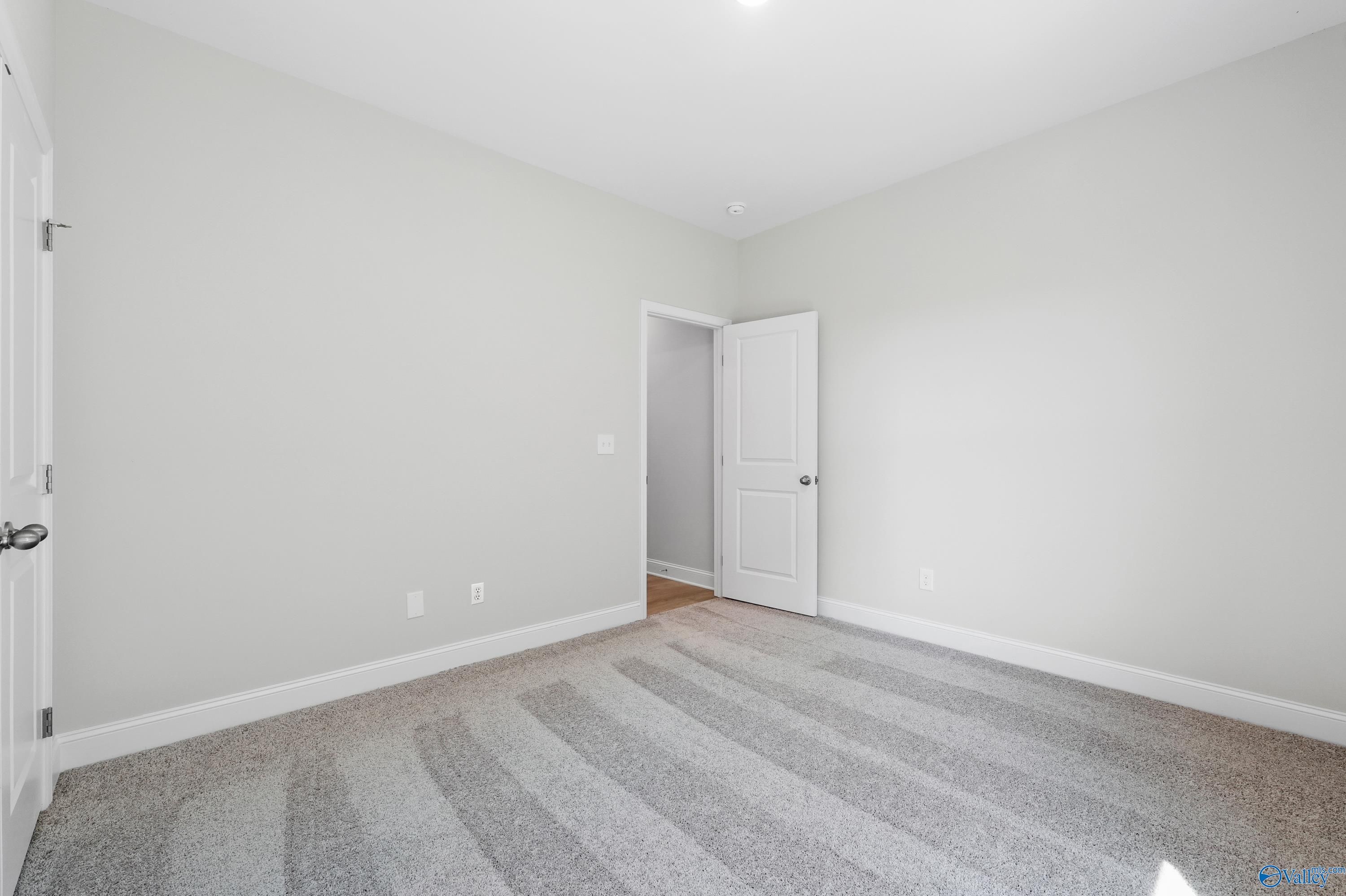 Empty secondary bedroom featuring light gray walls, white doors, and plush carpet in Davidson Homes The Everett, Hazel Green, Alabama
