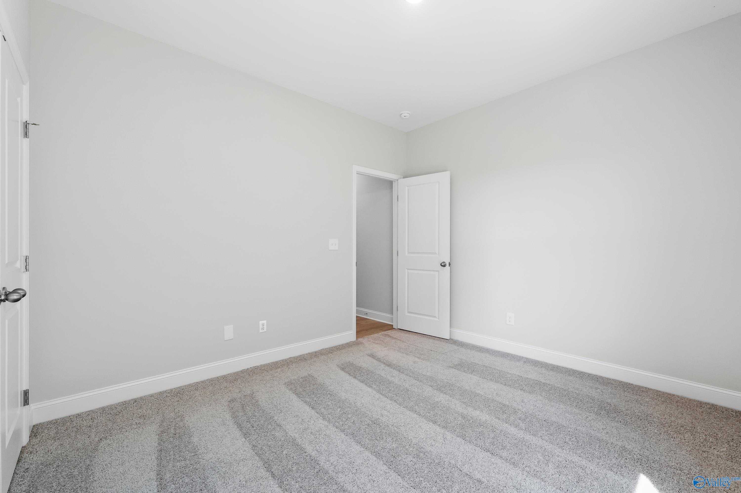 Empty secondary bedroom featuring light gray walls, white doors, and plush carpet in Davidson Homes The Everett, Hazel Green, Alabama