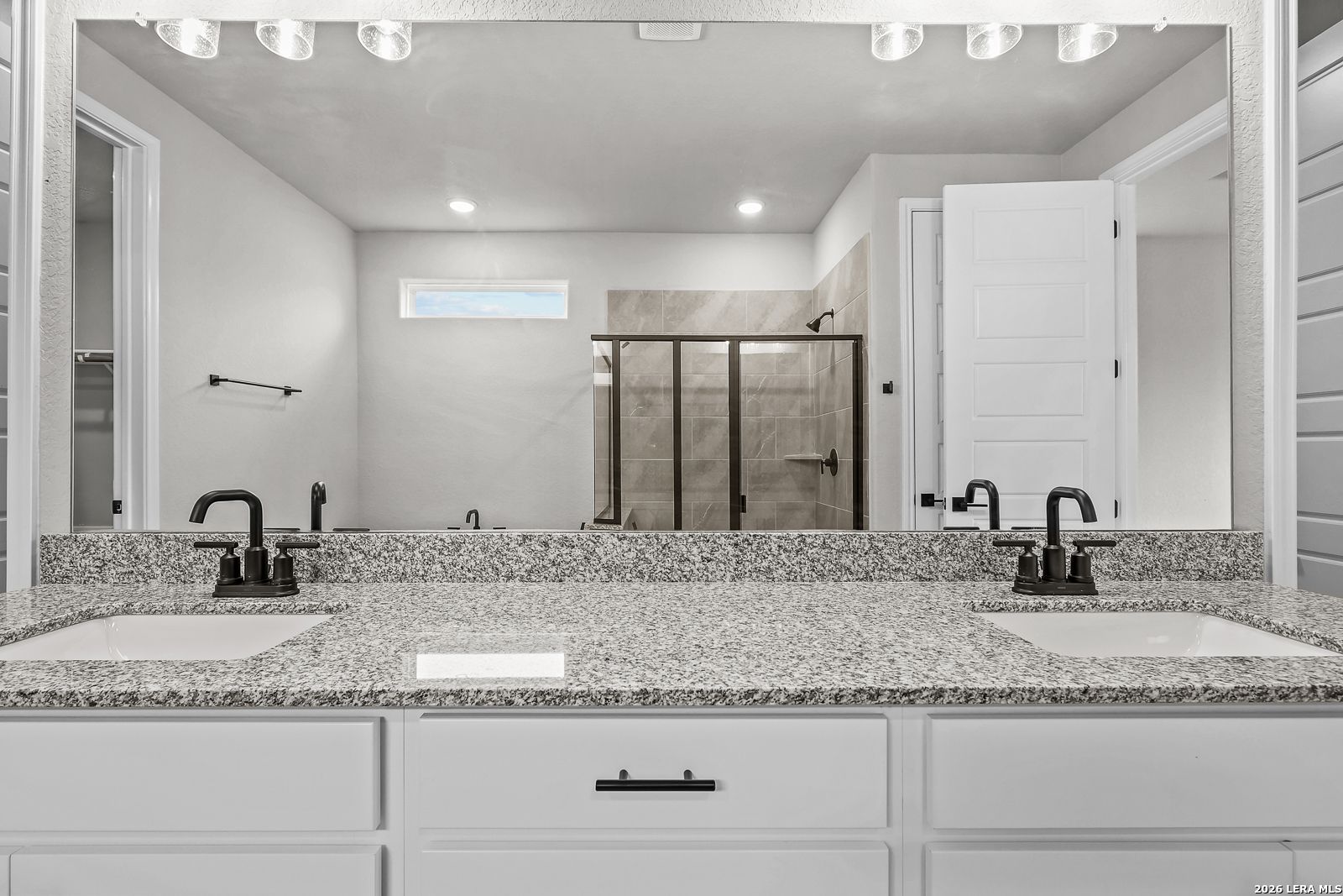 Modern master bathroom with double granite vanity, black faucets, frameless mirror, and glass shower in Davidson Homes The Belmont H, Castroville, Texas