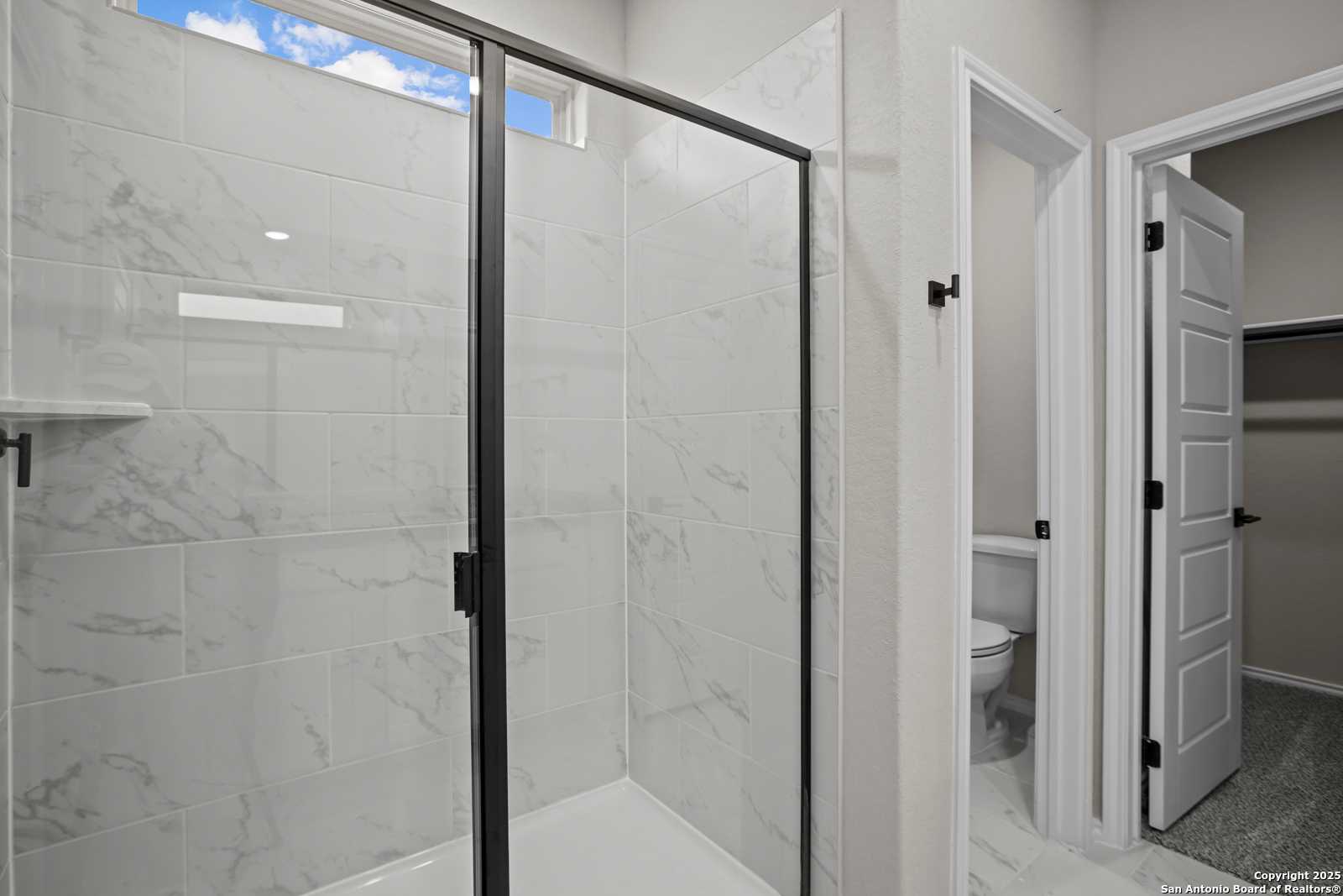 Modern frameless glass shower with white subway tile walls and adjacent toilet in Davidson Homes The Asheville E, Converse, Texas