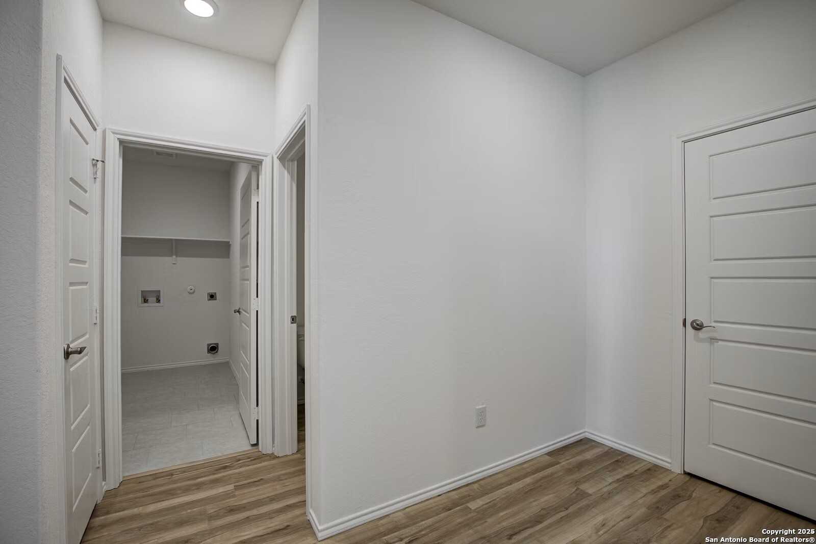 Bright laundry room with utility sink, hookups, and open doors on wood laminate floors in Davidson Homes The Douglas B, Seguin, Texas
