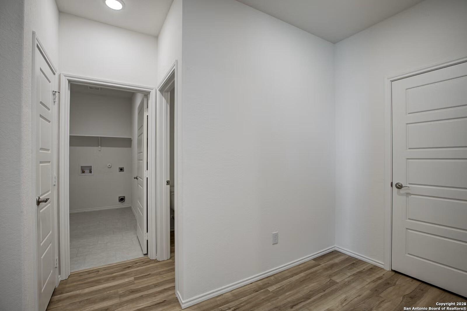 Bright laundry room with utility sink, hookups, and open doors on wood laminate floors in Davidson Homes The Douglas B, Seguin, Texas