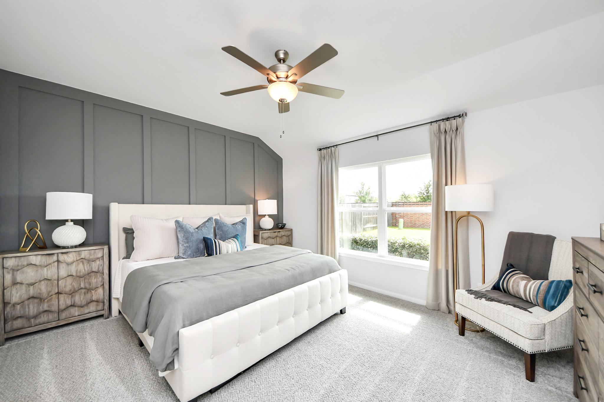Modern primary bedroom in Sunterra, Katy, TX, by Davidson Homes featuring a tufted bed and gray accent wall.