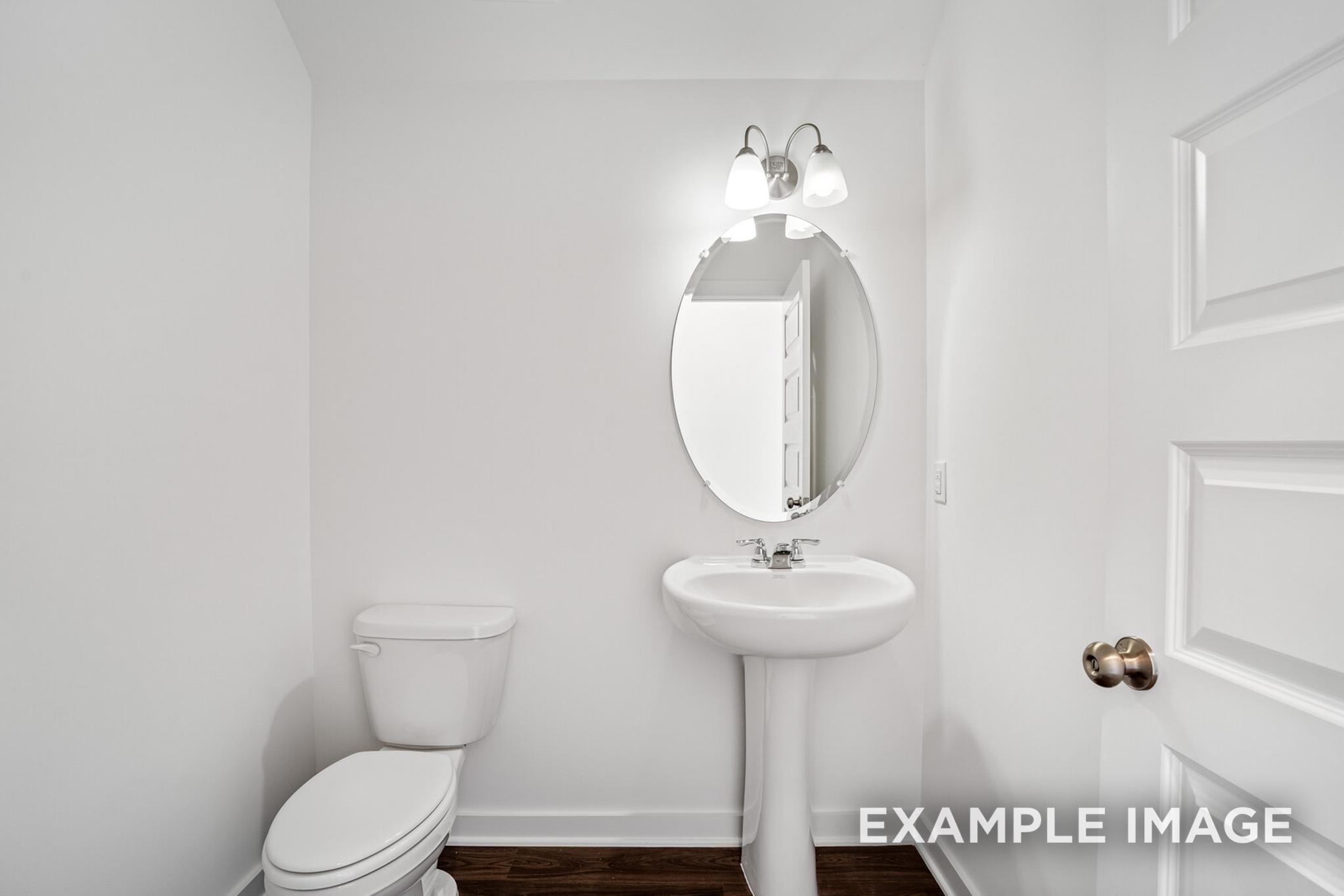 Compact powder room in The Logan C home design: white pedestal sink, oval mirror, toilet on hardwood floors, Davidson Homes