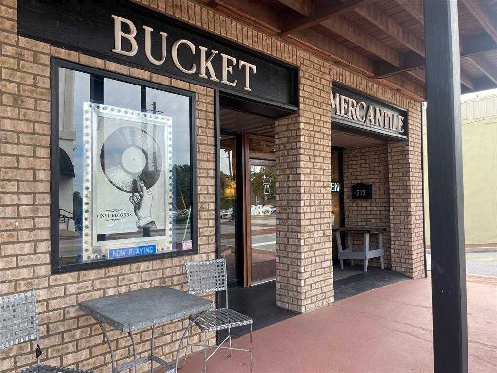 Charming Bucket Mercantile storefront exterior with vintage record poster in window, outdoor bistro table, and brick facade in Dallas, Georgia