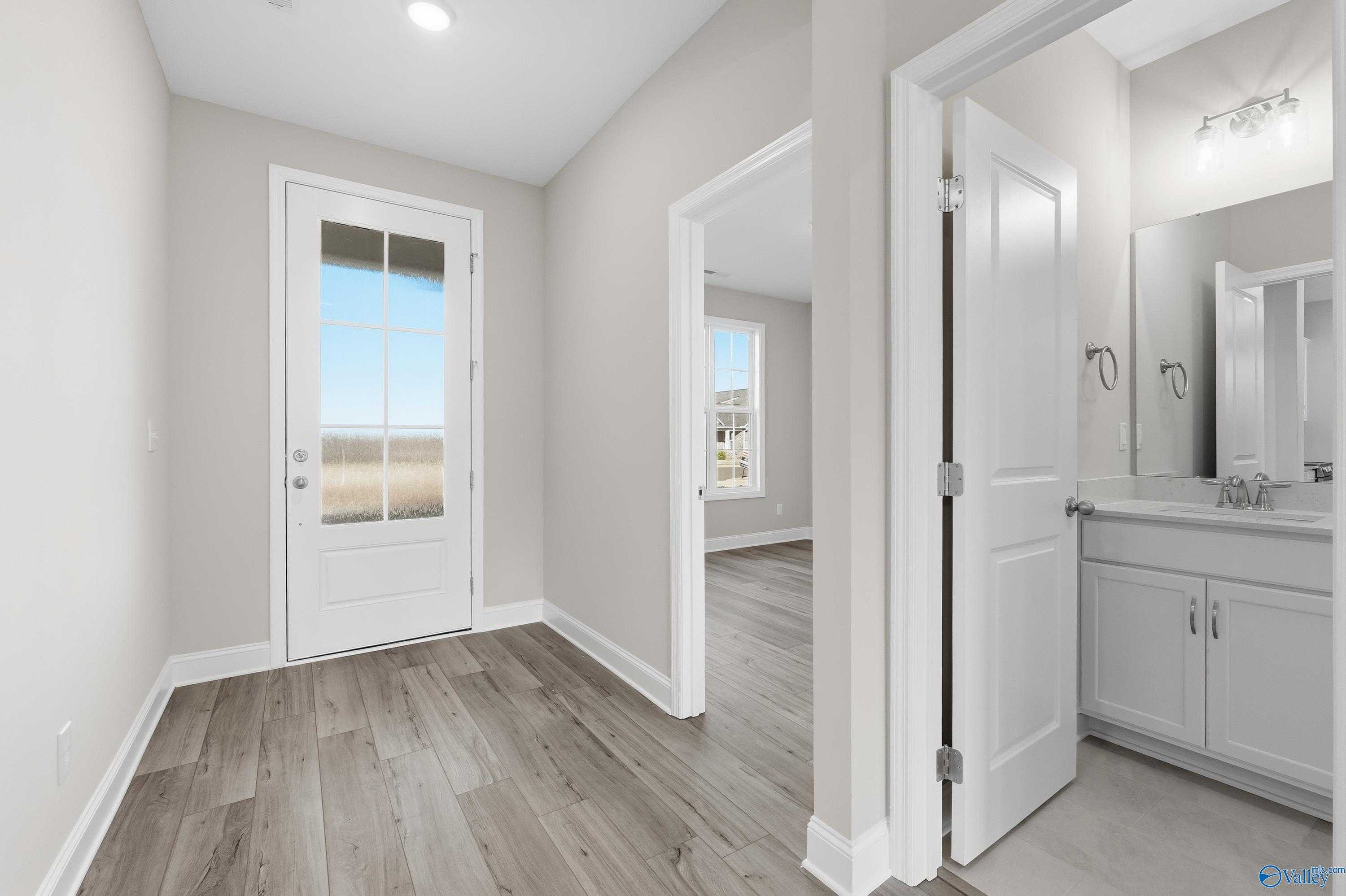 Bright mudroom with French door to backyard view and adjacent powder room with white vanity in Davidson Homes The Lanier, Toney, Alabama