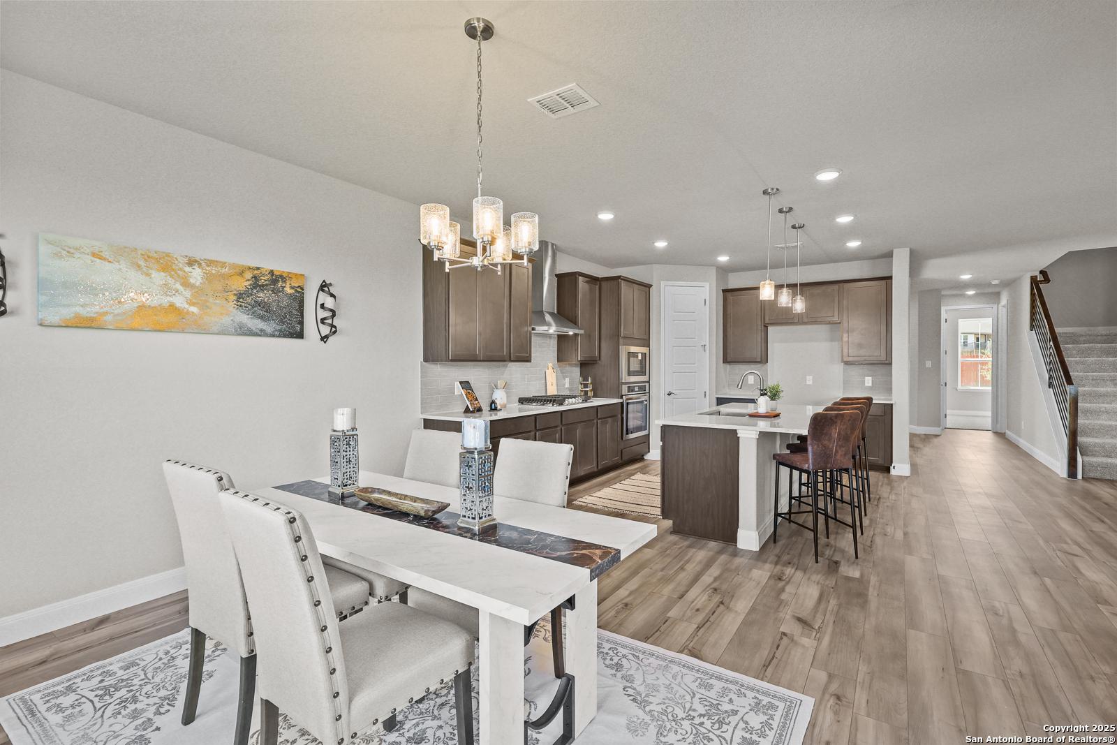 Open-concept kitchen with island, bar stools, and dining table in Davidson Homes The Jennings G, Castroville, Texas