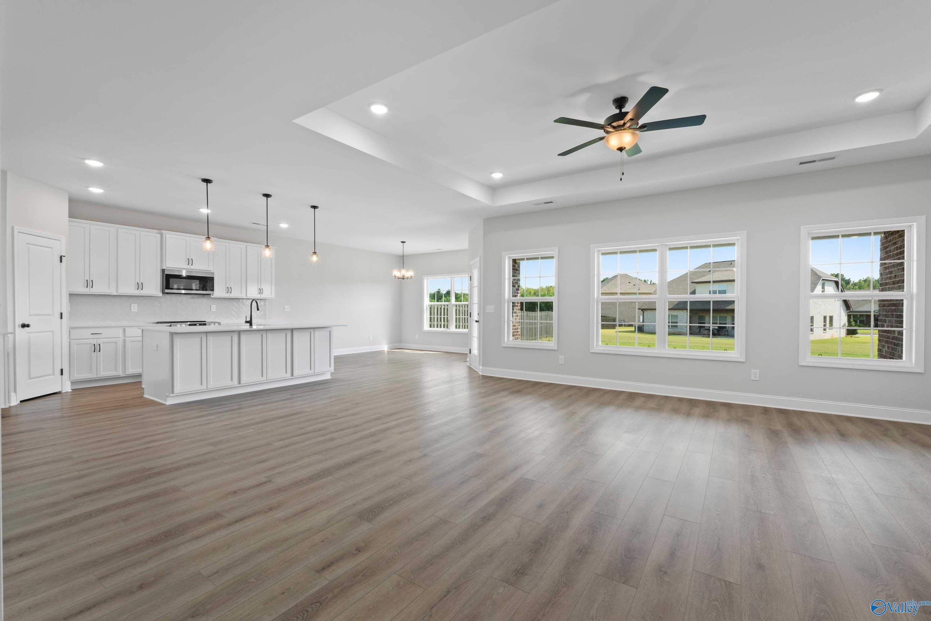 Open-concept kitchen with white shaker cabinets, large island, hardwood floors, ceiling fan, and backyard views in The Rockford home, Toney, Alabama