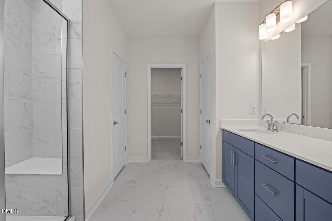 Modern primary bathroom with blue dual vanity, tiled walk-in shower, and walk-in closet in The Hickory II B, Montrose home.