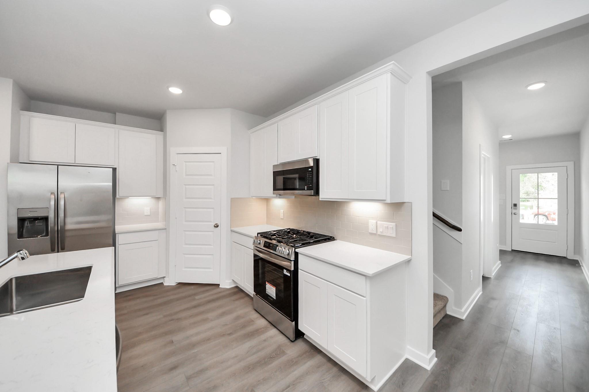 Modern white kitchen with stainless appliances, quartz countertops, and pantry in Davidson Homes Sabine F plan, Conroe, TX