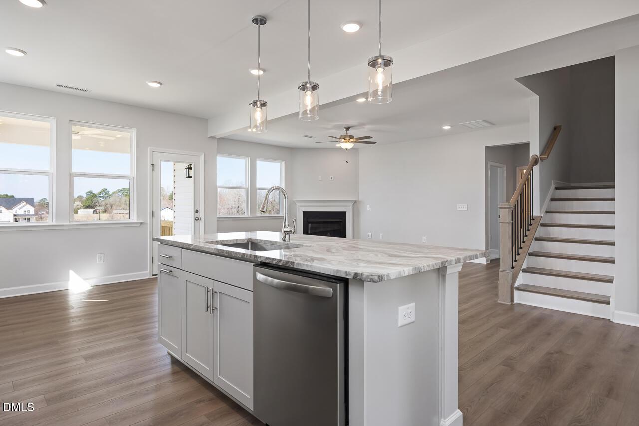 Modern open-concept kitchen with quartz island, stainless dishwasher, fireplace, and staircase in 5-bedroom Willow G home, Angier, NC